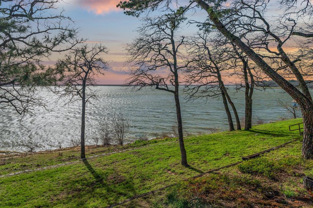 Set high above the shoreline on a commanding bluff overlooking Lake Grapevine, this rare 1.412-acre lakefront homesite offers 180-degree, southwest-facing lake views with spectacular sunset exposure. Spanning two lots at the end of a quiet street, the property combines exceptional privacy with a dramatic setting that feels expansive and serene. No HOA to limit the possibilities on this beautiful prime piece of waterfront land.
Offered as land, this is a rare opportunity to secure one of Flower Mound’s most compelling lakefront properties with the flexibility to build now, hold for the future, or bring your own builder—there is no obligation to build with any specific builder. Two existing homes currently on the property offer potential interim use while plans are finalized.
For buyers seeking a more streamlined path to a custom estate, the seller has partnered with Partners in Building on a concept for a two-story residence with a walkout basement, thoughtfully designed to capture lake views from nearly every level. See MLS 21224469 for additional build information.