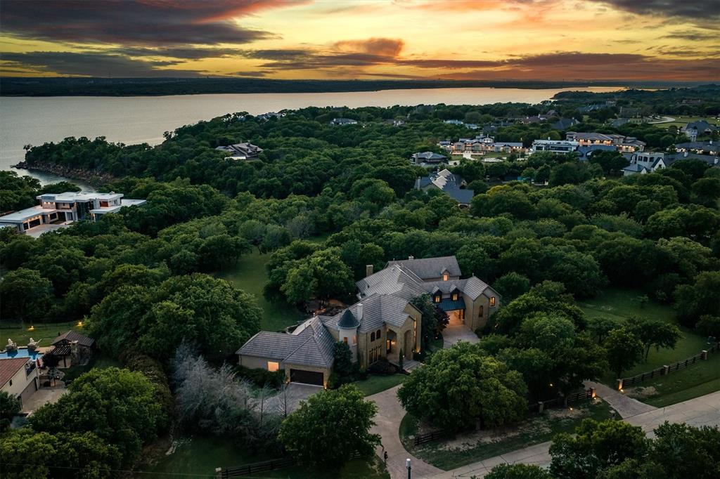 Tucked away on over 2 private acres, surrounded by multi-million-dollar estates, this 5-BR home w. no HOA beautifully blends luxury, comfort & natural beauty, backing to Army Corps of Eng. land along Grapevine Lake for exceptional privacy & serene views. Step thru the marble-tiled grand foyer w. soaring 2-story ceilings & immediately take in the view of the breathtaking backyard oasis. Rich woodwork, elegant chandeliers & 6 FPs create a warm yet sophisticated atmosphere thru-out this home. A car enthusiast’s dream: 4 garages (1 w. lift, 1 tandem) accommodate up to 8 vehicles. The private owner’s wing offers a primary suite w. tray ceiling, FP & sitting area overlooking the grounds. The spa-inspired bath features dual vanities, oversized shower, flows into an enormous custom WI closet. Just outside are a dedicated office & private garage access. In the opposite wing, a secondary suite w. sitting area, ensuite bath & WI closet sits across from the formal dining. A wet bar adjacent to the breakfast rm opens to the outdoor living via a convenient pass-thru window. The chef’s kitchen is fully equipped w. BI fridge, dbl ovens, 6-burner gas cooktop, expansive island w. prep sink & brkfst bar, all opening to a sunlit brkfst area. Triple stone arches lead to the living rm w. coffered ceiling, floor-to-ceiling stone FP, built-ins & walls of windows. Upstairs, a private wing features an expansive media rm w. wet bar. Down the hall, a 2nd family rm w. coffered ceiling & bar area opens to a balcony overlooking the pool & tranquil grounds. 3 additional BRs, 2 w. corner FPs & private balconies, feature ensuite baths & WI closets. A massive game room w. FP & wine bar is accessible via a staircase from the LR downstairs, while separate guest quarters include a living & kitchen area, full bath & private garage access.  Outdoors, unwind in the resort-style backyard w. covered patio, sparkling pool w. spa & grotto, a lush lawn framed by mature trees beyond.  Your own private sanctuary!