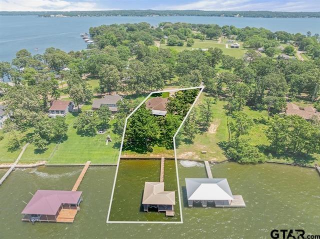 Experience refined lakeside living in this beautifully appointed waterfront residence, offering 1,949 square feet of thoughtfully designed space on a generous .34-acre lot with captivating open-water views. This three-bedroom, two-bath home seamlessly blends elevated comfort with modern sophistication, highlighted by soaring ceilings and tasteful updates throughout. The inviting living area serves as the heart of the home, anchored by a charming wood-burning fireplace and framed by scenic lake vistas. A light-filled sunroom provides the perfect setting for peaceful mornings and unforgettable sunset views, while the expansive covered deck creates an exceptional outdoor living space ideal for entertaining or relaxing in a tranquil setting. Designed with both convenience and functionality in mind, the property features a full-perimeter bug misting system extending to the boathouse, an extra-deep garage, oversized storage shed, and a spacious fenced backyard. A long private driveway offers ample parking for residents and guests alike. Boating enthusiasts will appreciate the private boathouse situated in deep water, complete with a new 10,000 lb. boat lift and the option to extend the dock. Located on the highly sought-after Lake Palestine, known for premier fishing and recreational boating, the community further enhances the lifestyle with a private boat launch and secure trailer storage. Ideally positioned for both privacy and accessibility, the property is located approximately 1.5 hours from Dallas, under 30 minutes from Tyler, and within three hours of Austin and Houston—making it a perfect primary residence or luxurious weekend escape.