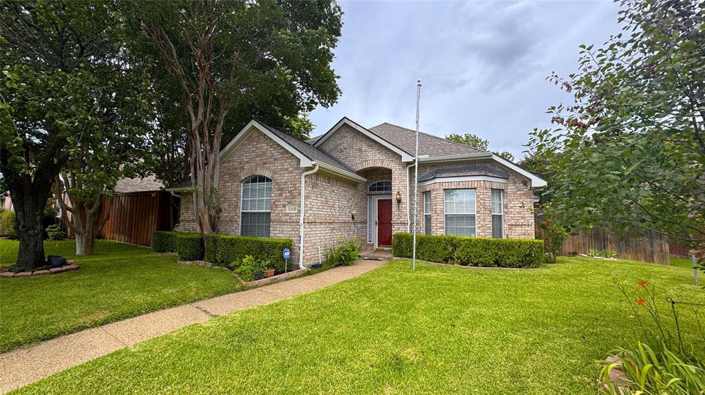 This single-story brick home features a functional layout and natural light throughout. The entry leads to a front flex room with a bay window, suitable for a home office or dining space. At the center of the home, the living room includes wood-look flooring, built-in shelving, and a fireplace. It flows directly into the kitchen, which offers painted navy cabinetry, a center island, a breakfast bar, and white appliances. The attached breakfast nook features a bay window and backyard access. The primary bedroom includes an arched window and an en suite bathroom with split dual vanities, a corner garden tub, and a separate shower. Two secondary bedrooms share a full hallway bathroom, and a dedicated laundry room provides built-in storage shelves. Outside, the fenced backyard features a wood deck and a covered patio surrounded by mature trees. The property is situated in an established neighborhood within walking distance of multiple playgrounds and a local elementary school. Residents will enjoy quick access to nearby grocery stores, restaurants, and shopping, as well as a short 15-minute drive to major area sports and entertainment venues.