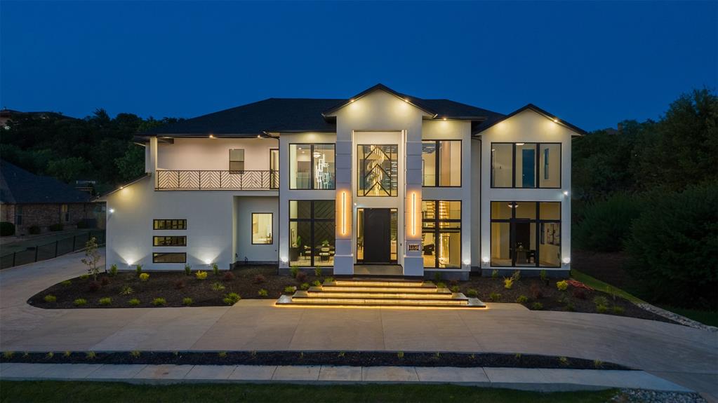 Architecturally striking modern contemporary estate situated on over 1 acre in the exclusive Lake Ridge community. This exceptional custom residence spans 5,300 square feet and offers soaring 12–26 ft ceilings, and meticulously curated designer finishes throughout. Expansive floor-to-ceiling glass frames breathtaking 180-degree panoramic metroplex views while flooding the home with natural light. An oversized front and exterior terrace provide a stunning backdrop for sunset evenings and city skyline displays.
Designed for elevated living and effortless entertaining, the open-concept interior is anchored by a dramatic floating staircase with illuminated treads and sleek glass railings. A glass wine cellar with ambient LED lighting adds an impressive architectural focal point, while oversized 9-ft panoramic sliding doors seamlessly blend indoor and outdoor living spaces for full use of outdoor kitchen and covered patios. 
The chef’s kitchen is a true statement piece featuring a 10-ft Cristallo quartzite waterfall island, custom ceiling-height cabinetry, premium appliances, and an elegant prep pantry with secondary sink.
Luxury amenities include a private cinematic theater with a 100-inch linear fireplace, integrated Sonance in-ceiling audio throughout the residence and outdoor living areas, and a full security camera system. The lavish primary retreat offers coffered ceilings, and a linear fireplace, creating a true resort-inspired atmosphere. The spa-caliber ensuite bath features a wall-mounted heated towel rack, oversized walk-in shower, soaking tub, dual vanities, and separate his-and-hers water closets for ultimate comfort and privacy. 
Completing the estate is an oversized 4-car garage with lift-ready capability for up to 6 vehicles, EV charging readiness, and extended depth designed for oversized trucks or vehicle storage. A grand circular drive enhances the home’s commanding curb appeal and provides ample guest parking.
