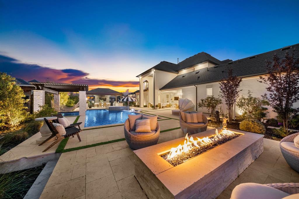 Featuring over $550,000 in seller upgrades, this exceptional home is situated on an oversized cul-de-sac lot with a private gated drive and porte cochère, offering both privacy and striking curb appeal. A grand foyer with a dramatic double staircase, custom millwork, designer lighting, and decorative wall paneling sets the tone for the thoughtfully designed interior adding warmth to each space. Off the entry, a private office with custom built-in cabinetry creates the ideal work-from-home space, while the formal living room and butler’s pantry seamlessly connect to the heart of the home. The expansive main living area is highlighted by soaring two-story ceilings, wood beams, a floor-to-ceiling fireplace, and a second-story balcony overlooking the kitchen and living spaces, creating an open atmosphere filled with natural light. The designer kitchen is beautifully appointed with gourmet appliances, custom finishes, and an oversized island that anchors the space for both entertaining and everyday living. High-end indoor and outdoor sound equipment with integrated speakers throughout elevate the entertaining experience. The downstairs primary suite offers a true retreat, featuring elegant coffered ceilings, separate double vanities, dual walk-in closets, a soaking tub, and a walk-in shower. A secondary downstairs bedroom with an ensuite bath provides the perfect setup for guests or multigenerational living. Upstairs, you’ll find a spacious media room, game room, and two additional ensuite bedrooms, offering privacy and flexibility for family and guests alike, along with a large walk-in storage space that could easily be converted into a fifth bedroom. Designed for both relaxation and entertaining, the resort-style backyard is truly unforgettable. Enjoy tranquil water and fire features, a heated pool and spa, relaxing hammocks suspended over the water, a full outdoor kitchen, and multiple outdoor seating areas that create the ultimate indoor-outdoor living experience.