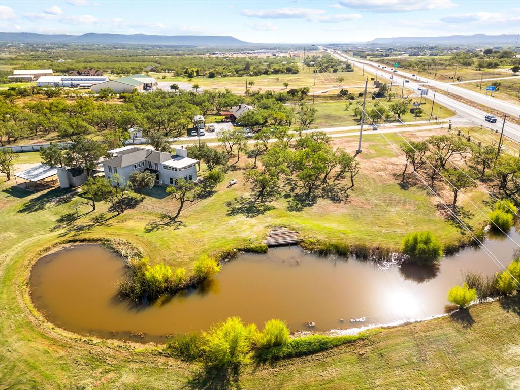 This one of a kind property offers space, character, and endless potential on 5 beautiful acres with prime highway frontage just outside of Abilene. With 3,486 square feet, 4 spacious bedrooms, and 3 bathrooms, this home is ready for its next chapter. Inside, you will find two large living areas that create flexibility for entertaining and relaxing. The main level features a cozy fireplace, while the upstairs living space is centered around a charming wood stove. The second upstairs bedroom opens to a balcony overlooking the property and offers peaceful West Texas views. Outside, the possibilities continue. A large tank adds to the natural beauty of the land, while goat pens and open space make it ideal for a small hobby farm or simply enjoying country living with room to roam. The excellent highway frontage also creates exciting potential for a home based business or future commercial use. This property presents a great opportunity for buyers with vision to update, personalize, and create something truly special. Whether you are looking for a private retreat, an investment opportunity, or a unique place to call home, this property is full of potential.