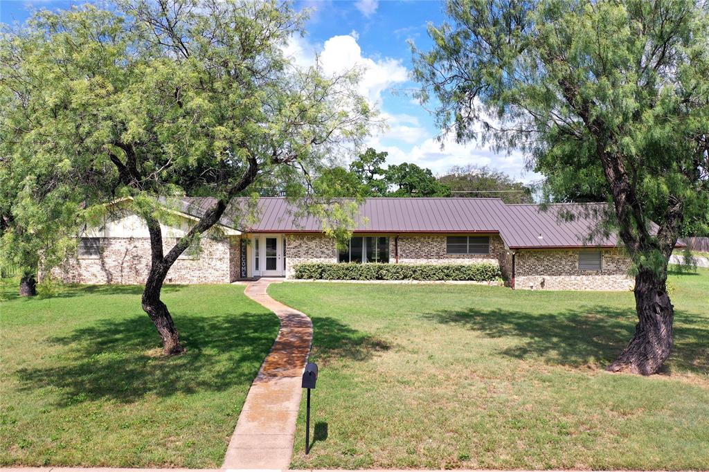 Welcome home to this spacious 4-bedroom, 2-bath residence situated on a desirable corner lot in the heart of Jacksboro, Texas. Offering approximately 1,946 square feet of comfortable living space, this property combines small-town charm with room to grow.
Inside, you'll find a thoughtfully designed floor plan featuring generous living areas, ample natural light, and plenty of space for family gatherings and everyday living. The four bedrooms provide flexibility for a growing family, home office, guest accommodations, or hobby space.
The home sits on an oversized lot measuring approximately 137.5' x 145', just under one-half acre, providing abundant outdoor space for recreation, gardening, entertaining, or future improvements. The rear-entry two-car garage enhances curb appeal while offering convenient access and additional parking options.
Step outside and enjoy a beautifully shaded backyard featuring mature trees, a landscaped flagstone-covered patio, and partial wrought iron fencing that adds both character and openness to the outdoor living space. Whether you're hosting family barbecues, enjoying a quiet morning coffee, or simply relaxing in the shade, this backyard offers a welcoming retreat.
The brick veneered home with its sharp looking standing seam metal roof; maintenance will no longer be an issue!  Whether you're looking for extra room inside and out or seeking a well-located property with a large lot, this Jacksboro home offers a wonderful opportunity to enjoy comfortable living with plenty of space to make your own.