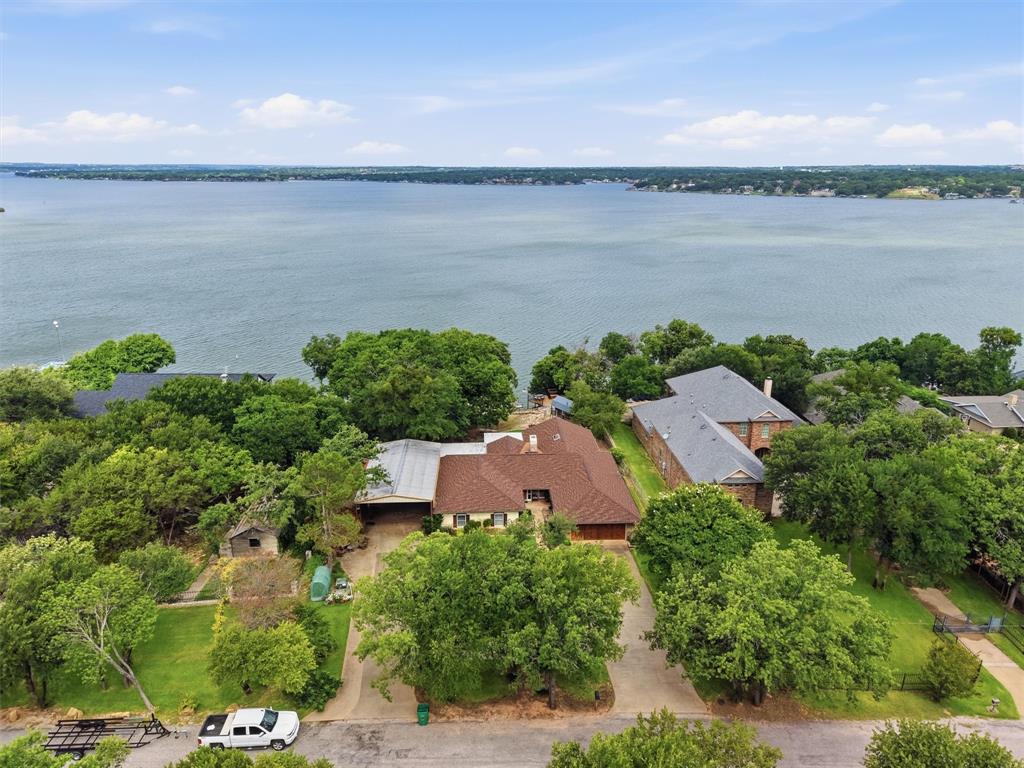 Experience exceptional lakefront living with this beautifully maintained single-story waterfront home offers breathtaking open-water views, timeless character, and exceptional privacy beneath a canopy of mature oak trees. Expansive windows fill the home with natural light while framing panoramic lake vistas from the main living areas, all opening to a spacious covered porch designed for year-round entertaining and unforgettable sunsets.  Inside, expansive windows fill the home with natural light while showcasing the spectacular setting. The living and dining areas flow effortlessly into a spacious kitchen featuring abundant workspace, breakfast bar seating, and uninterrupted lake views. Multiple sunrooms provide year-round enjoyment regardless of the season. The generous primary suite serves as a private retreat with serene water views and direct access to a lakeside sunroom.  Outside, professionally terraced landscaping and native stone walkways lead to the shoreline, where a lakeside cabin creates the perfect guest retreat, hobby space, or private waterfront escape. Access to the lake is available by both a private tram and a scenic stone pathway. The impressive multi-level dock features two boat slips, a storage room, a rooftop entertainment deck overlooking miles of open water and 30'+ deep waters ready for you to dive in!  Additional amenities include an air-conditioned 10x16 custom workshop with built-in workbenches, a separate 10x16 storage building, a covered RV carport with full hookups and a raised garden area ideal for gardening enthusiasts and fruit trees.  This is truly a special opportunity to experience the very best of Lake Granbury living.