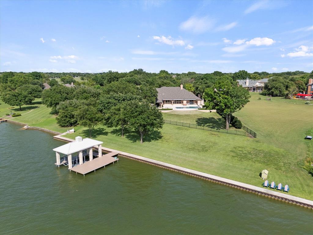 Waterfront estate resting on 1.65 acres with pristine 200 feet of Lake Ray Hubbard shoreline with seawall offering panoramic lake views. Expansive vistas of sunsets and sailboats. Boat house with boat lift and 2 waverunner lifts. Perfect for motorboat or jet skis. Grecian-style pool is surrounded by lush, groomed grounds with seating areas. Outdoor covered living space with fireplace. The grand entry welcomes you with exquisite elegance and versatile design. Large open living and entertainment areas. Sand and finish. Herringbone pattern wood floors. Gourmet chef's kitchen is culinary experience. Separate large Butler's Pantry. Second living area plus a theater room. Primary suite is a true ensuite hosting its own living area with a fireplace, separate entry to the pool and spectacular lake views. Second primary bedroom upstairs. All bedrooms have ensuite bath. Flex room upstairs for multi-uses including a 5th bedroom. Two separate garages, 8 car spaces; 1 garage has workshop and more valuable storage space. Stately gate entrance leads to private drive which presents a country feel but is close to all of the conveniences. HURRY! This jewel box won't last long
