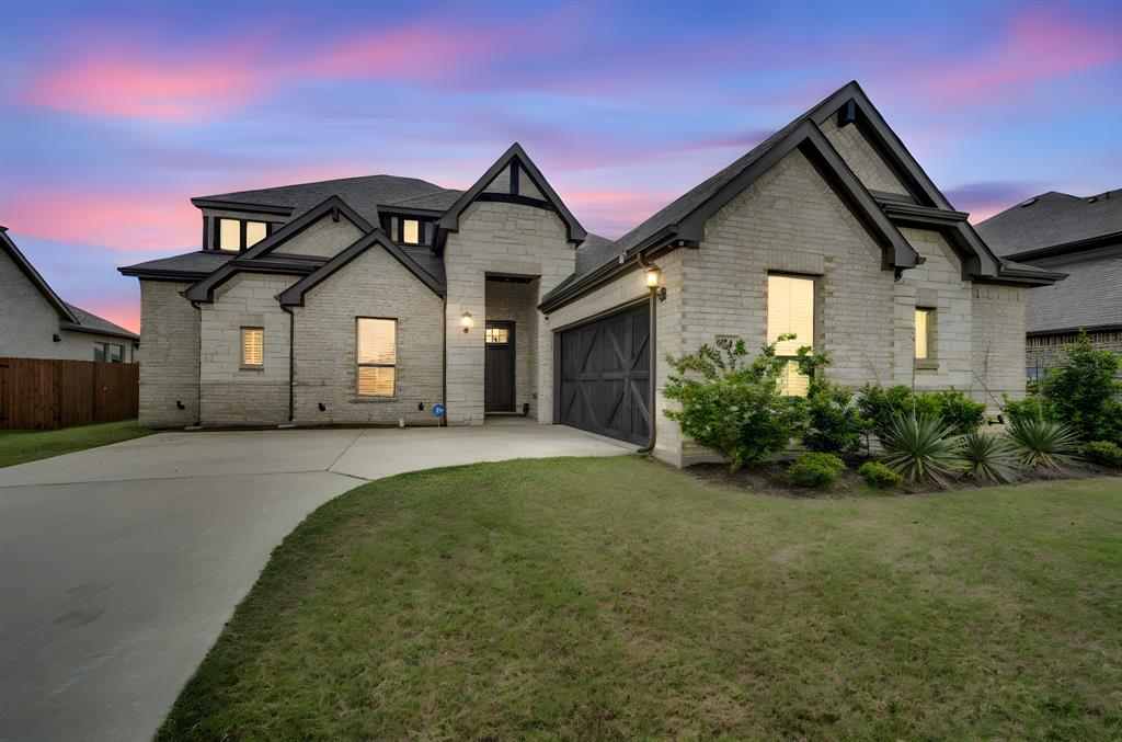 JUST REDUCED!!! Stunning Tudor-inspired home featuring crisp limestone exterior, dramatic dark trim, and charming barn-style garage door with exceptional curb appeal. Step inside to a grand foyer with tray ceiling and engineered hardwood floors flowing throughout the open-concept main living area. The chef's kitchen impresses with floor-to-ceiling white cabinetry, quartz island with seating, gray subway tile backsplash, stainless appliances, and a dedicated coffee-butler's bar. The expansive living room opens seamlessly to the kitchen and dining area — perfect for entertaining. Retreat to the spa-like primary bath boasting dual vanities, soaking tub and separate walk-in shower. With high ceilings, abundant natural light, and designer finishes throughout, this gem blends modern farmhouse elegance with everyday comfort. The generously sized lot offers endless outdoor possibilities — plenty of room to add a resort-style pool, playground, or open space for kids and pets to roam freely. Schedule your private showing today — homes like this don't last long!