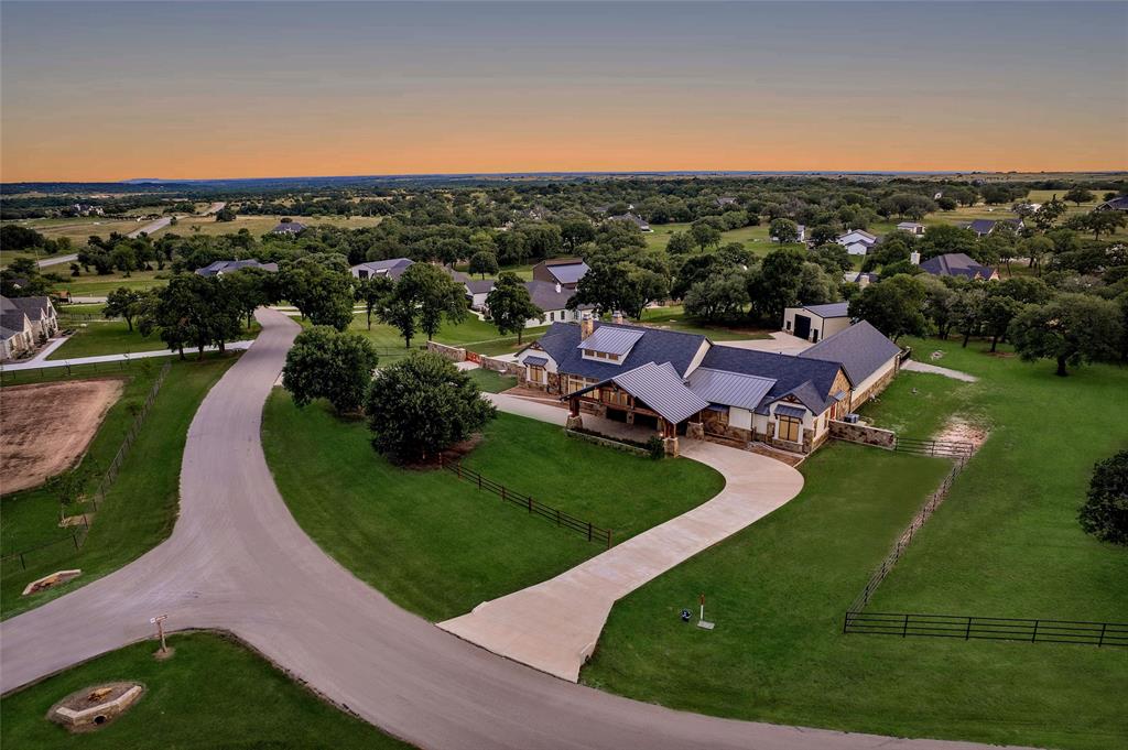 Welcome to 117 Hansma Way, a breathtaking custom ranch estate in the gated Bar H Ranche community of Weatherford. Set on 2 ACRES of picturesque Parker County land with mature trees and full PIPE fencing, this property captures the heart of horse country living with true Big Texas energy. Every aspect was crafted with care and precision. Meticulously maintained and still presenting like new, this retreat is designed for comfort, beauty, and peace of mind. The residence offers nearly 4,809 square feet with 4 bedrooms, 4 full baths, and 1 half baths, plus a full bath in the 30×40 workshop. Interiors showcase hand-scraped hickory wood floors, travertine tile, masonry fireplaces, and onyx lighting. HEATED bathroom floors add luxury, while wide hallways, handicap rails, and wheelchair-friendly design provide accessibility. A private MOTHER-IN-LAW SUITE with private living room offers space for guests or multi-generational living. The gourmet ENTERTAINING kitchen is both elegant and practical, featuring an oversized island, double ovens, warming oven, gas stove, two dishwashers, two sinks, wine cooler, and walk-in pantry. Built with integrity, the home includes 2x6 insulated walls, insulated ceilings and interior walls, Class 4 hail-resistant shingles, a 40–45 kW Generac GENERATOR, 1,000-gallon buried propane tank, three zoned HVAC units, and a tornado-rated safe room with 14-gauge steel walls. Even the garages, attic, and workshop were insulated and finished with care. Two oversized 2-car garages with epoxy floors, EV charger, custom storage, and a porte-cochere are paired with a 30×40 insulated WORKSHOP with full bath. Outdoor living shines with a covered kitchen including grill, pellet smoker, refrigerator, sink, and burner, plus an expansive patio with fireplace. Every inch of this estate reflects craftsmanship, foresight, and pride of ownership, offering a rare opportunity in one of Weatherford’s top small-acreage luxury communities. More details at 117hansmaway.info