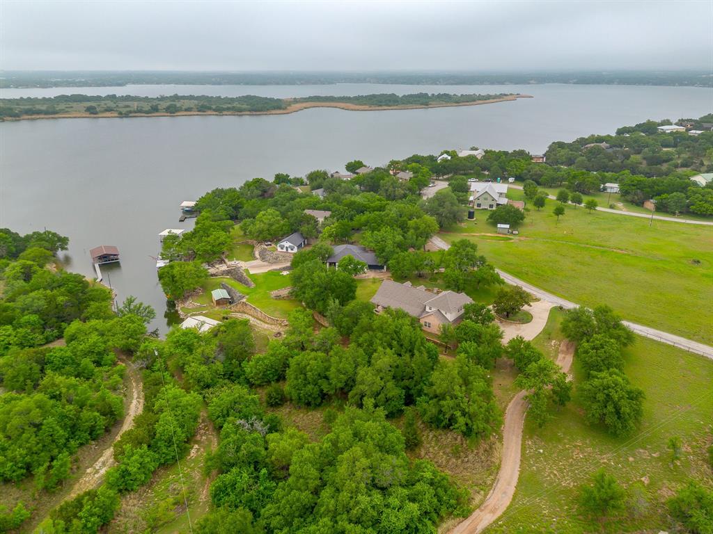 Set on a quiet, private stretch of waterfront on the Fort Worth side of Lake Granbury, this rare custom home offers the ideal balance of seclusion, accessibility, and a beautiful view of the lake. Positioned in a protected cove with a clear sightline to the main body of water, the property delivers both calm shoreline living and scenic water vistas. Built in 2012 by Couto Homes, this fully custom 4-bedroom, 3-bath home was thoughtfully designed with oversized walkways and doorways to provide ease of movement and wheelchair accessibility throughout. The open-concept floor plan is anchored by expansive floor-to-ceiling windows that frame the lake, filling the home with natural light and uninterrupted views. The main living area features a gas fireplace and flows seamlessly into the kitchen and dining spaces, creating an ideal setup for both everyday living and entertaining. The primary suite is located on the main level and includes a private exterior door leading directly to the wraparound porch, perfect for quiet mornings or evening lake views. Outdoor living is a standout feature, with a wraparound porch spanning three sides of the home (excluding the garage side), offering multiple vantage points to enjoy the water and surrounding landscape. The 1.29-acre property consists of three parcels, with the main parcel currently benefiting from an agricultural exemption.
Additional highlights include: Private well water; Lake-fed sump pump for the sprinkler system; Covered dock with space for a boat and jet skis; Extensive stone retaining walls that terrace beautifully down to the water’s edge.
Located within a small, low-impact HOA community, this property offers a rare opportunity to own a private, well-built waterfront home with both functionality and timeless design. Schedule your private showing today to experience this exceptional lakefront property in person!