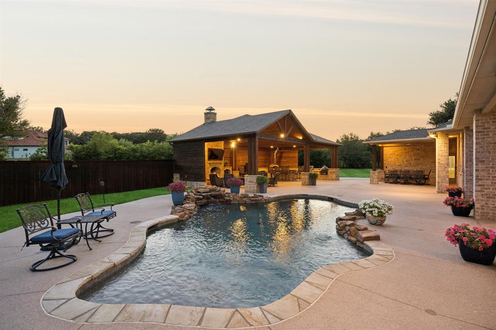 Tucked beneath a canopy of mature trees on two beautifully landscaped acres, this impressive single-story estate makes a striking first impression upon arrival. The dual gated entrances and an expansive circular drive offer convenience, privacy, and ample parking for guests and entertaining, while the tree-lined setting creates a peaceful, estate-like retreat. An extraordinary backyard showcases a massive custom pavilion with soaring vaulted tongue-and-groove ceilings, stunning stone fireplace, authentic wood-fired pizza oven, built-in grill, bar with island seating, and even a separate pool bath. Sparkling saltwater pool with natural stone waterfall offers multiple resort-style lounge and dining areas, making this outdoor oasis the ultimate setting for summer gatherings to fall evenings by the fire and feels like a private luxury getaway beneath the Texas sky. Featuring  the Main Residence, measuring 3,010sqft and a second guest quarters, measuring 404sqft.  Main residence highlights include an expansive open-concept living & chef-inspired kitchen area with rich custom cabinetry, granite countertops, double ovens, a gas cooktop, and oversized center island. Adjoining living room features a floor-to-ceiling stone fireplace with custom built-ins and abundant natural light. Primary suite is perfectly placed for serene pool views and direct access to the covered patio. Additional spaces include a dedicated home office with hardwood flooring, an oversized formal dining space and two additional bedrooms with jack & jill bath. Guest Quarters is outfitted with a kitchenette, full bath, and private entrance. Perfect for multigenerational living, private guest accommodations, home gym, or studio. Lastly, the property also features an expansive four-car garage with abundant storage space. Offering the perfect balance of luxury, privacy, and resort-style living in one of Copper Canyon’s most desirable settings. Denton ISD. Low Tax Rate of 1.8188%