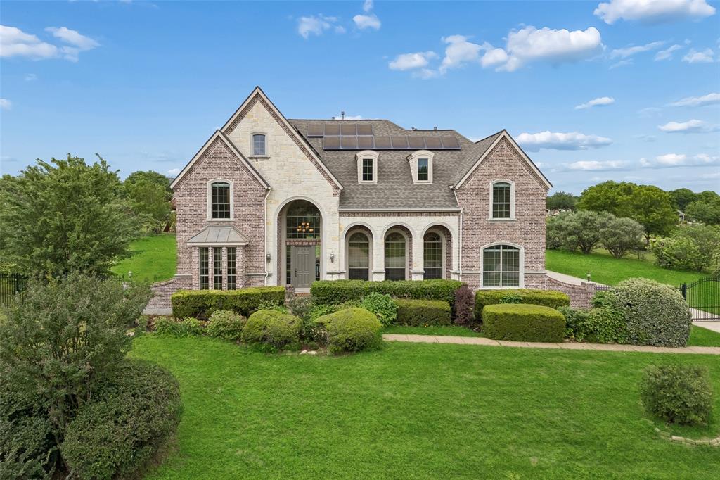 Set on an acre behind a private gated entrance and directly across from the neighborhood lake, this one-owner Drees custom home offers genuine privacy, generous proportions, and ultra-low utility expenses. A grand two-story foyer with curved staircase, hand-scraped hardwoods, and iron-balustrade rail opens to formal living and dining rooms with crown molding and abundant natural light. The two-story family room features a wood-mantel fireplace, custom built-ins, and a soaring wall of glass that frames the expansive backyard and treetops beyond. The kitchen offers rich wood cabinetry, granite counters, dual islands with cooktop and prep space, stainless built-in appliances, and a turret breakfast nook with panoramic backyard views. A fully built-in study and a powder bath complete the main level. The downstairs primary suite is a quiet retreat with a curved wall, tray ceiling, and sitting area with art niche; its spa-style bath features dual granite vanities, a jetted corner tub, separate shower, and oversized walk-in closet. Upstairs, three generous secondary bedrooms (one en-suite, two sharing a Jack-and-Jill) sit beside a large game room with wet bar and wine storage, plus a tiered media room with projector and surround sound included. Recent and notable updates include fresh paint and new carpet throughout, many new windows, a Class 4 impact-resistant roof for added durability and potential insurance savings, fully owned Tesla Powerwall and rooftop solar for substantial utility savings, a three-car garage, and full yard irrigation. The level, fully fenced backyard offers room for a future pool, sport court, or outdoor kitchen, framed by mature shade trees with long sightlines across the property. A quiet street, a lakeside setting, and a move-in-ready home that shows even better in person.