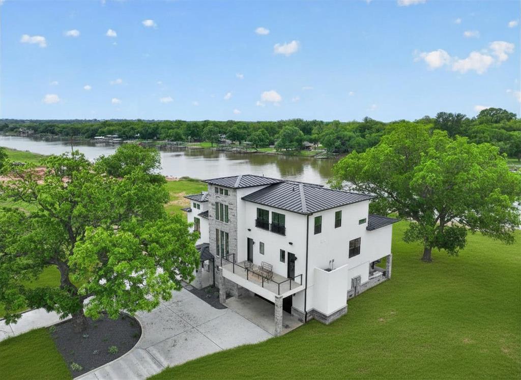 Introducing an extraordinary modern estate in River Ranch on the Brazos, the DFW area’s premier gated waterfront community. Inside, warm contemporary design & high-end finishes create an unforgettable experience. White oak flooring, complemented by custom white oak cabinetry in the kitchen, primary suite & main living. Expansive living room is anchored by a porcelain-wrapped fireplace, while oversized windows flood the home with natural light. Chef’s kitchen is a true showpiece, featuring premium KitchenAid commercial-grade apps including a built-in refrigerator + freezer, 36-inch gas range, under-counter microwave & beverage refrigerator. A dramatic waterfall island is topped w-Broadway Black quartz counters in a leather finish, paired with a full-height matching backsplash & sleek floating shelves for a clean, modern aesthetic. Primary suite was designed as a private retreat, complete with dual walk-in closets & French doors opening to the 2nd floor patio. Spa-inspired primary bath offers vaulted ceilings w-a designer chandelier, separate floating vanities with Taj Mahal quartzite countertops + a stunning Japanese soaking tub. Designed for both entertaining & everyday living, the home also features a custom spiral staircase connecting the main living area to the outdoor kitchen, a private 1st floor office for added work-life separation, a 3rd-floor reading nook perfect for kids & even a private elevator spacious enough for multiple guests. Thoughtful additions such as a whole-home water filtration system + a secure safe room w-a metal vault door provide peace of mind. Outside, the resort-inspired outdoor kitchen & pool bath showcase imported Italian porcelain finishes, while the striking bright white stucco & charcoal stone exterior create unforgettable curb appeal. Set within an exclusive gated community, River Ranch on the Brazos offers private boat slips, panoramic waterfront views & a lifestyle centered around luxury, privacy & unforgettable family memories.