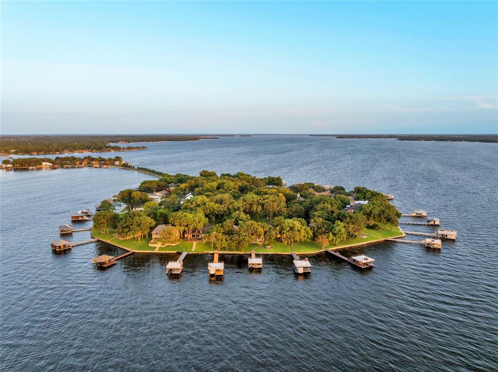 Welcome to your dream retreat on Cedar Creek Lake! Located in the prestigious, gated community of Enchanted Isle, this stunning lakefront home features four spacious bedrooms, including a luxurious primary suite and a convenient secondary bedroom on the ground floor. The downstairs boasts soaring 12-foot ceilings, creating an airy, open atmosphere.  A magnificent wall of windows offers breathtaking views of the tranquil lake, flooding the home with natural light and connecting it seamlessly to the serene outdoors. Positioned on the island, the property is sheltered from summer south winds and provides spectacular sunset vistas. The recently renovated dock enhances the outdoor living experience, featuring a boat lift and a lift for two wave runners. Whether entertaining guests or enjoying a peaceful evening by the water, this exceptional home on Enchanted Isle blends luxury, comfort, and natural beauty perfectly.