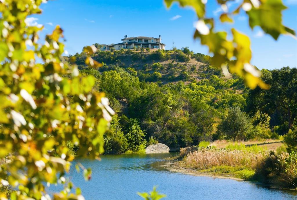 Extraordinary 855-acre live-water ranch in the heart of the Texas Hill Country, located 15 minutes west of Dripping Springs, 2.5 miles from Highway 290, & approximately 45 minutes from downtown Austin. The property features nearly 1.5 miles of spring-fed Mustang Creek, flowing year-round—even in drought conditions—& dammed to create multiple deep lakes ideal for fishing, swimming, & paddleboarding. The renowned vineyard region (between Johnson City & Fredericksburg) is just 30 minutes away, as well as Wimberley. The land showcases dramatic elevation changes, with rolling valleys and commanding hilltops that deliver sweeping panoramic views in every direction. Crowning one of these hilltops is a 7,000 sq ft custom residence offering six bedrooms & seven bathrooms, thoughtfully upgraded with new hardwood floors, a fully updated kitchen, an elevator, a dedicated wine room, & a Savant AV control system. Outdoor living is equally impressive, with a negative-edge pool & expansive entertaining areas that take full advantage of the surrounding vistas. Privacy is paramount, with access provided by a gated, one-mile private paved road, & the entire ranch is high fenced. A large pond greets you at the entrance, & wildlife is abundant throughout the property. The ranch is managed under a wildlife plan and includes 10 deer feeders, six turkey feeders, & six established food plots, supporting a thriving habitat. Additional improvements near the creek include a two-bedroom, one-bath foreman’s house, a rustic three-bedroom, two-bath guest home, a well-designed equestrian facility, & a large equipment barn. Whether envisioned as a recreational retreat, hunting ranch, legacy estate, or private sanctuary, this property represents a rare offering that captures the very best of Texas ranch living and is a once in a generation opportunity for a ranch of this size and quality this close to Austin. Additional 2,300 plus or minus acres available; see Agent for more information.