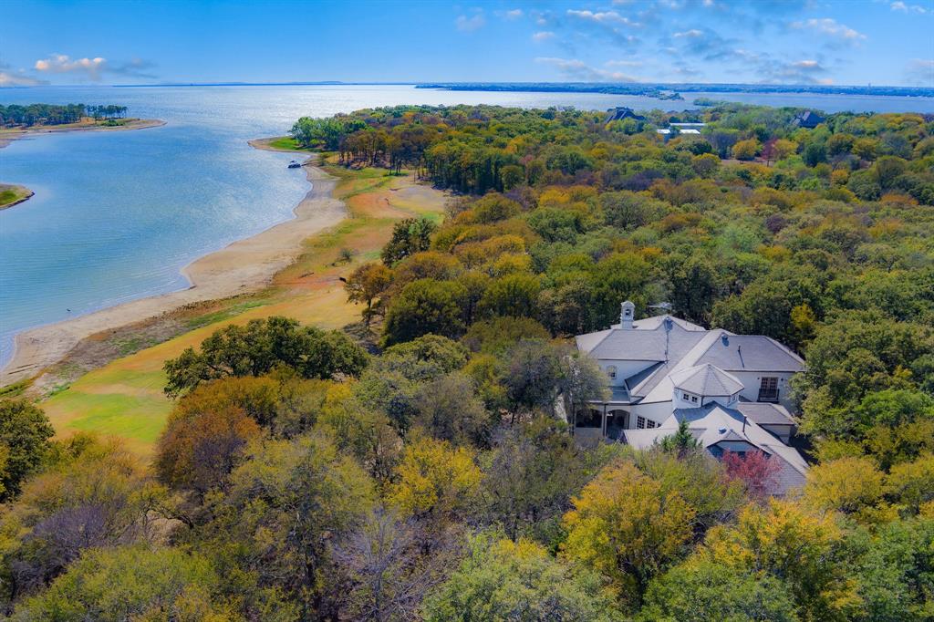 Experience Lewisville lakefront living on this private gated 5-acres! A Mediterranean style home, Ag exempt (Only $11,571 annual tax) w livestock. Heavily treed acreage inside city limits 10 min from Frisco & 20 min from DFW airport. Roof, gutters Oct2022. 2-story hall with spiral staircase to flex living space on either side formal living and dining rooms. Chef's kitchen, entertaining island and built-in fridge. Double-sided fireplace that flows from great room to sunroom, offering lake views from every room. Extremely rare 228 feet of private beachfront, perfect for relaxing on the sand or enjoying water activities like kayaking and paddle boarding. As the new owner, you can add floating a dock of your choosing for easy lake access. Whether you're a boating enthusiast or enjoy the peace and tranquility of the water, this property offers endless opportunities for outdoor recreation and relaxation. Don't wait to schedule a viewing and make this lakefront paradise your new home today!