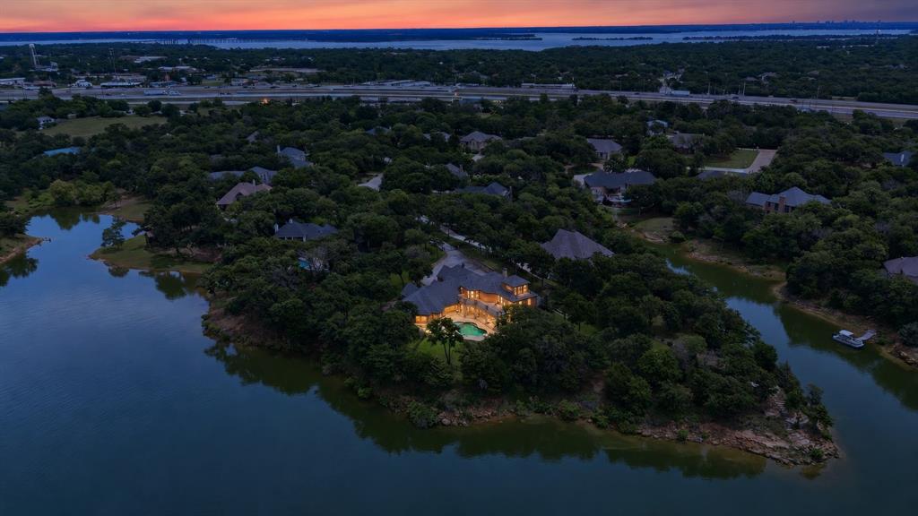 Welcome home to 7 Hillview Court in the sought after neighborhood of Shore Haven! This custom estate commands a picturesque 1.4-acre waterfront lot on a peaceful finger of Lake Lewisville. Tucked away at the end of a quiet cul-de-sac and surrounded by lush landscaping and mature trees, this private sanctuary delivers an immediate wow factor. Upon opening the front door, you are greeted by direct views of the pool and Lake Lewisville. The heart of the home is designed for grand-scale entertaining. The kitchen features SS commercial-grade appliances and flows into the expansive living room. Here, exquisite workmanship is on display, highlighted by hand-scraped hardwood floors, a vast stone fireplace, and a spectacular rotunda ceiling with intricate inlaid wood. An executive study boasts a coffered ceiling, while the media room promises ultimate movie nights. The main floor also hosts a massive game room featuring a stone-chase fireplace and a wet bar, making indoor-outdoor hosting seamless. The main-level primary suite offers stunning views and privacy from the large secondary bedroom suite down. Upstairs provides an exceptional layout for family or guests, featuring two additional large secondary bedrooms. Both bedrooms have direct access to an amazing oversized balcony patio, offering panoramic views of the rolling lawn and lake. A spacious landing area provides the perfect breakout zone for reading or watching TV, positioned next to the exercise room. For the ultimate escape, ascend the winding staircase to the third-floor Eagles Nest. Complete with its own private balcony, this unique space serves as an inspiring secondary study, reading room, or star-gazing observatory. Outside, the resort-style backyard features a sprawling covered living space, saltwater pool, and a 4 car garage. This outdoor oasis is fully equipped for ultimate efficiency and peace of mind, featuring a dedicated irrigation system sourced directly from the lake alongside a home generator.