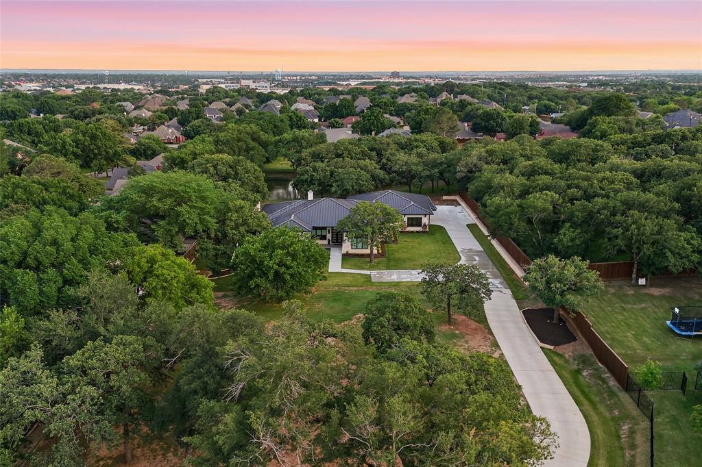 Welcome to 6717 Brazos Bend— Completed in May 2025, an exceptional custom-built, single-story estate just minutes from Colleyville, offering a rare combination of privacy, acreage, resort-style pool, and luxury living. Situated on nearly 1.5 acres across two combined lots, the property offers mature trees, tranquil pond views, and a level of seclusion that is increasingly hard to find. Designed for both everyday comfort and entertaining, the outdoor living experience is a highlight. The heated pool and spa are complemented by a fully equipped outdoor kitchen and covered living area, all positioned to capture the natural beauty of the property. Inside, the home showcases a seamless blend of craftsmanship and functionality. Open-concept living spaces are anchored by a Napoleon Vector gas fireplace, custom cabinetry, and expansive glass sliders creating a seamless indoor-outdoor connection. The gourmet kitchen features a large island, Wolf and Sub-Zero appliances, a convection steam oven, pot filler, and a butler’s pantry with additional refrigeration and storage. The thoughtfully designed floor plan includes four bedrooms, each with a private bath, along with a dedicated study featuring custom built-ins and white oak beams. A versatile game or media room offers flexibility for entertaining or relaxing while  overlooking the backyard. The private primary suite serves as a true retreat with a spa-inspired bath featuring a double shower, soaking tub, lava rock sinks, & luxury finishes. Additional features include wide plank white oak flooring, motorized Hunter blinds, inset cabinetry, a standing seam metal roof, multi-zone HVAC, a security system, cool storage room 17x6, utility-workshop 23x9, & a three-car garage. Located just minutes from top-rated schools, dining, shopping, and major commuter routes, this home offers the perfect balance of peaceful living and convenience. 6717 Brazos Bend is a rare opportunity to own a private, estate-style property near Colleyville.