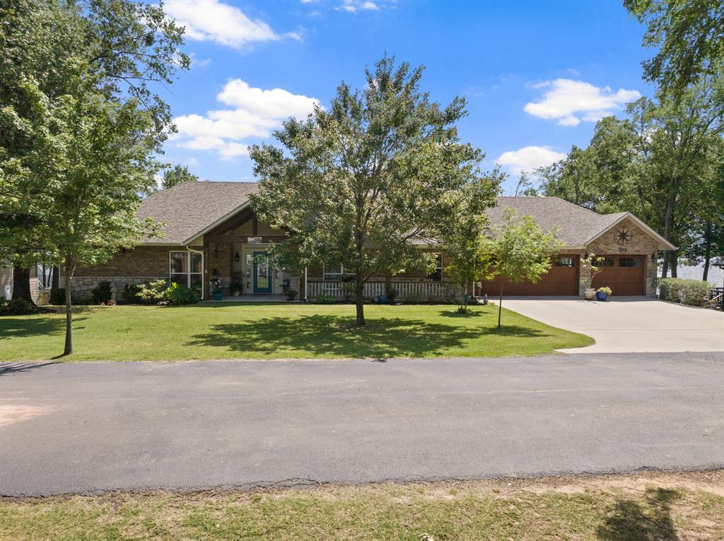 Welcome to this exceptional waterfront retreat on Lake Bob Sandlin, where refined comfort meets effortless lakefront living. Tucked inside a gated community, this stunning custom-built home offers over 2,700 square feet of thoughtfully designed space, perfectly positioned on a beautifully maintained lot with direct water access. From the moment you step inside, you’re greeted by soaring vaulted ceilings and a breathtaking wall of windows that floods the home with natural light and frames picturesque views of the lake. The open-concept living area is designed for both relaxation and entertaining, anchored by warm finishes and seamless indoor-outdoor flow. The chef’s kitchen features a large island, breakfast bar, double ovens, and an abundance of cabinetry, opening effortlessly into the main living and dining spaces—ideal for hosting family and friends. The private primary suite offers a serene escape, complete with a spacious layout and a spa-like ensuite featuring a jetted tub, separate shower, and generous walk-in closet. Additional bedrooms provide comfort and flexibility with a Jack and Jill bath, all conveniently located on a single level. Step outside to expansive covered and open decking, where you can unwind, entertain, and take in the peaceful waterfront setting. The property also includes a boathouse, making lake days effortless and accessible year-round. There is plenty of storage for your water toys in the spacious room under the house. With a three-car garage, quality brick and stone construction, and a location in one of the area’s most desirable lake communities, this home offers the perfect blend of luxury, privacy, and lifestyle. Experience the best of Lake Bob Sandlin living—where every day feels like a getaway.