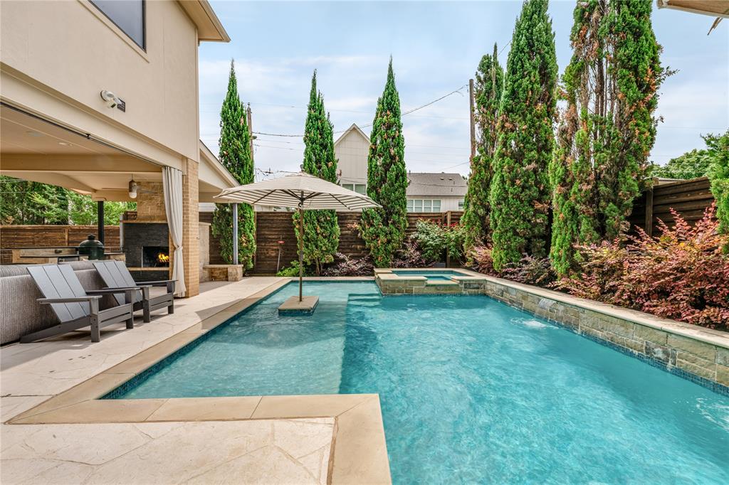 Situated in one of Lakewood’s most serene and walkable pockets, this beautiful home blends rich, moody design with warm, inviting living spaces just moments from White Rock Lake, the SoPac Trail, and highly sought-after Lakewood Elementary. The outdoor living experience is exceptional, made to feel like a private resort tucked into one of Lakewood’s quietest and most peaceful settings. A covered patio with fireplace creates a true year-round outdoor living room, overlooking the pool and spa with an oversized tanning deck and tranquil waterfall features. The outdoor kitchen is fully equipped with a built-in grill, Big Green Egg, and two generous seating areas. Just off the patio, a convenient half bath adds functionality for pool days. The yard is framed with lush landscaping and enhanced by a sliding rear gate for added privacy and expanded yard space. From the moment you step inside, the expansive foyer and soaring two-story ceilings create an unforgettable first impression, flooding the home with natural light. The home features a handsome office with tall ceilings and custom built-ins, a formal dining room anchored by a striking glass wine cellar wall, and a purposeful mud room and built in desk area. The breakfast nook has been reimagined as a cozy lounge-style retreat overlooking the outdoor living area, creating the perfect setting for morning coffee or evening cocktails. Upstairs, an oversized media and game room combination offers flexibility, featuring a projector, bar area, and mini fridge ideal for movie nights, entertaining, or play space. Recent updates since 2024 include a brand new class 4 roof, all new cool stone on the patio, new cabinet hardware in kitchen and all baths, all new plumbing fixtures, new thermostats, all new light switches, new microwave, some new windows, new bathroom grout throughout, new garage storage systems. New washer and dryer from 2024 and media room projector stay with the home.