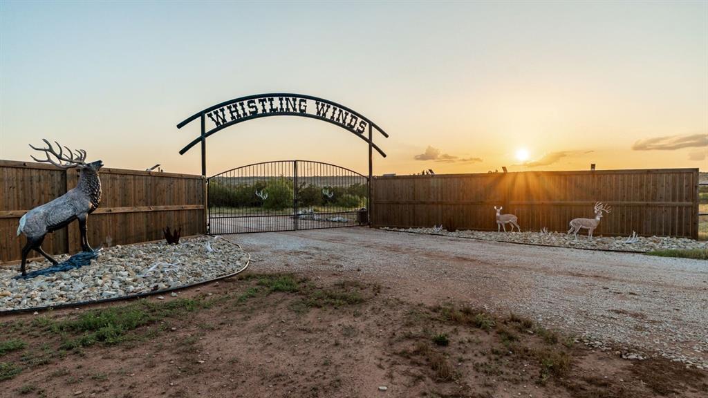 Whistling Winds Ranch is one of the most unique and breathtaking properties in North Texas. From dramatic elevation changes to custom-built lodges and lakes, every aspect of this ranch captures the true essence of luxury, recreation, and adventure.

The ranch features a one-of-a-kind 80’ x 80’ barndominium lodge that serves as both a comfortable retreat and a fully functional headquarters. With 2,000 square feet of living space, this lodge includes a trophy-lined great room, an impressive rock bar with a commercial-grade cooler and ice maker, and two guest suites with private baths. The wrap-around porches and outdoor firepit provide the perfect setting for entertaining or relaxing after a long day outdoors. The adjoining 60’ x 80’ insulated shop area offers four automatic rollup doors, industrial shelving, and ample storage.

Just west of the lodge, the custom cedar main residence overlooks the scenic Devils Creek canyon. The home features three bedrooms, a loft, three baths, vaulted ceilings, a wood-burning stove, and expansive windows showcasing the landscape. Its open kitchen with granite countertops and premium appliances makes it ideal for entertaining, while covered porches on the east and south sides offer stunning sunrise and sunset views.

The ranch’s terrain boasts over 200 feet of elevation change, unveiling canyons, creek bottoms, and sweeping views of the Pease River Valley. Three beautiful lakes—Devils Creek, Rock Lake, and a newly constructed western lake—offer incredible fishing and scenic tranquility.

Whistling Winds Ranch is high-fenced and home to an extraordinary mix of native and exotic wildlife including whitetail, mule deer, elk, red stag, fallow, aoudad, oryx, and more. With extensive road systems, food plots, and premium blinds and feeders, the property is turnkey for hunting, recreation, or private enjoyment.

This exceptional ranch combines luxury, functionality, and unmatched natural beauty—making it a true North Texas gem.