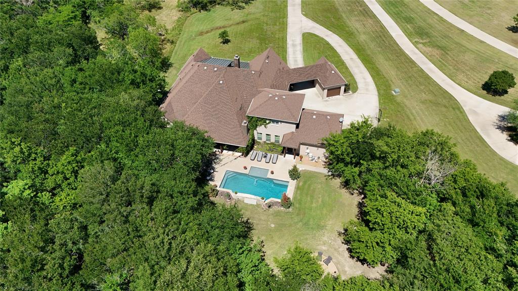 If you’ve been searching for a home that feels like a retreat without sacrificing luxury, this one delivers. Set on a beautifully wooded lot, this exceptional custom home showcases timeless craftsmanship and thoughtful design at every turn. The stone exterior and welcoming front porch make a lasting first impression, while inside you’ll find designer tile, custom cabinetry, and stunning stonework throughout. Exposed beams and arched accents add warmth and character, creating a space that feels both refined and inviting. The kitchen is built for connection, featuring a large island, abundant storage, and custom finishes that anchor the home. The primary suite offers peaceful views of the surrounding trees, along with a spa-like bath and spacious walk-in closet. Generously sized secondary bedrooms and two additional living areas provide room to spread out, entertain, or simply relax. A versatile bonus room above the garage gives you the flexibility to create whatever your lifestyle needs. Outside, the backyard transforms into a private oasis with a pool, fireplace, extended patio, and mature trees offering both beauty and privacy. Electrical outlets throughout the trees make adding lighting simple and seamless. A storm shelter and extra garage space round out the home’s thoughtful features. 
This one-of-a-kind property blends luxury, comfort, and nature into a home designed to be both lived in and loved.  You don't want to miss it.
