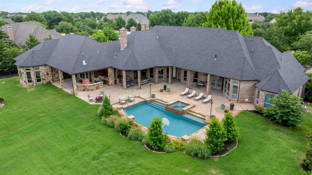 On 1.86 acres in an established ESTATE neighborhood, this custom home showcases exceptional craftsmanship, flexible living spaces, and resort-style outdoor amenities. Separate private staircases ensure easy access to the media and upstairs bedroom retreat while architectural details include tray ceilings, custom baseboards and trim, solid wood doors, and plantation shutters throughout. Up lighted tray ceilings in the family room, foyer, and primary suite create a refined ambiance, complemented by custom paint selections and designer finishes. The home offers 6 bedrooms, 6.5 baths, and an oversized 5 car garage. Also featured is a separate state of the art gym with full bathroom, accessible by the back patio. This unique space can easily be converted into a mother-in-law suite, office or bedroom if preferred. The gourmet kitchen features granite countertops, preparation space, top tier appliances and opens to the family room with a wood-burning fireplace. Designed for entertaining, the home includes a temperature-controlled wine cellar with wet bar, ice maker, and surround sound. The primary suite features a dual-sided gas fireplace and a flex space ideal for an office, nursery, sitting area, or expanded closet. The outdoor living shines with an extended covered patio featuring stained wood ceilings, ceiling fans, fireplace, and wood storage niches, kitchen area with a sink, refrigerator, grill, pizza oven, oversized pot burner perfect for crawfish boils, and extra storage. Additionally, the pool and spa feature a PebbleTec finish, slate stone landscaping, and gas lighting. Full exterior lighting and a comprehensive security system enhance ambiance and peace of mind. The property is fully fenced and backs to a creek and open space with no neighbors behind offering privacy and true ESTATE living in Prosper, TX. The home lives much like a single story with bonus space upstairs. Please access the gym from the back patio doors. Near Restaurants, Shopping, Highways.