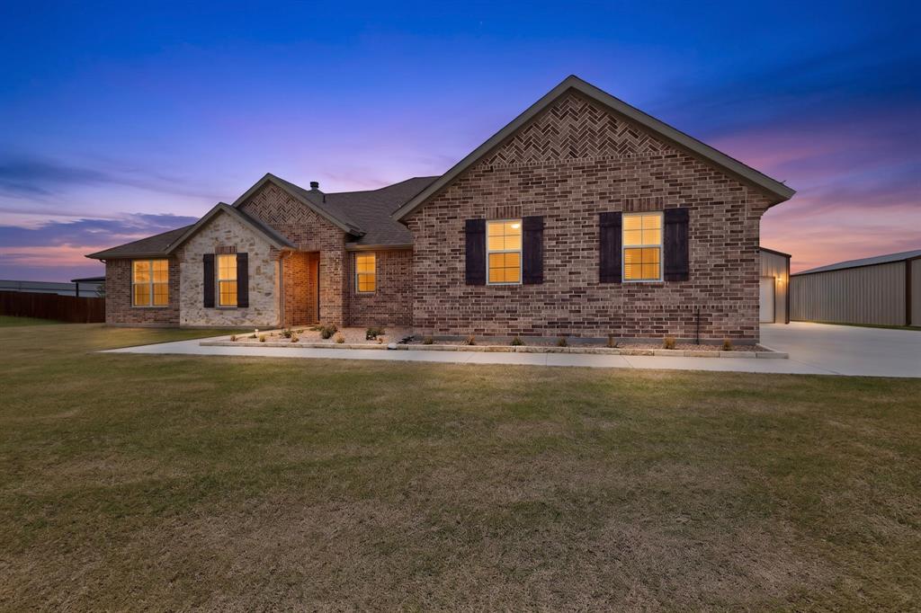 Experience the perfect blend of country tranquility and modern convenience in this like-new brick-and-stone single-story home situated on nearly one acre. Ideally located just minutes from Interstate 20, shopping, dining, and the outlet mall, this property offers the peaceful lifestyle you've been seeking without sacrificing accessibility. Outdoor enthusiasts will appreciate the neighborhood walking and biking trails, along with nearby Robert LaRue Park for recreation and leisure. A standout feature of this property is the newly constructed 22' x 40' workshop, with a steel frame structure, 12-foot sidewalls, soaring 16-foot peak ceiling, red steel support columns, an 18'x8' automatic overhead door, 100-amp electrical service, and multiple outlets—perfect for hobbies, projects, storage, or additional vehicle space. The expanded driveway leads to both the three-car garage and workshop, providing ample room for extra vehicles, recreational equipment, or a bass boat. Inside, the open-concept floor plan offers comfortable everyday living and effortless entertaining. A versatile front flex room serves perfectly as a home office, playroom, or additional living space. The gourmet island kitchen features quartz countertops, stainless steel appliances, a farmhouse sink, and abundant workspace. Adjacent to the kitchen is an oversized mudroom with a built-in workbench that connects to the spacious laundry room with storage. Privately situated at the rear of the home, the owner's retreat offers a relaxing escape with dual vanities, a walk-in shower, private water closet, and a walk-in closet. The thoughtfully designed split-bedroom layout places two secondary bedrooms on the opposite side of the home, connected by a shared full bath. Step outside to the expansive covered patio overlooking the large backyard—a perfect setting for entertaining family and friends or simply unwinding with your favorite beverage while enjoying the peaceful surroundings and wide-open Texas skies.