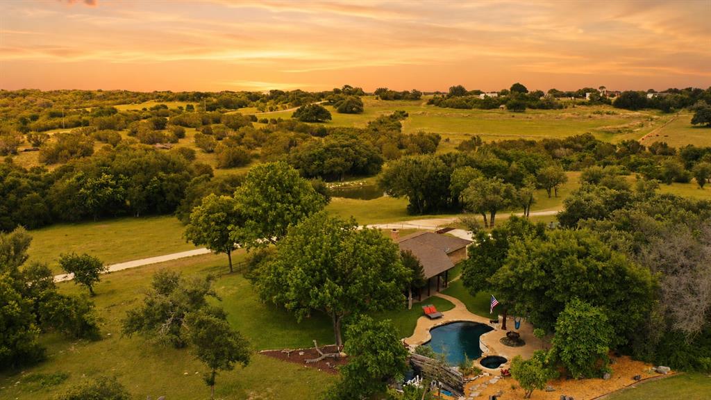 Meticulously maintained acreage retreat with a true Texas Hill Country feel, gorgeous views in every direction, and 36.42 acres just outside Stephenville. Currently ag exempt per seller, this 4-bed, 2-bath all-electric home offers a blend of comfort, recreation, and functional country living, with convenient proximity to Tarleton State University and an easy drive to the Dallas-Fort Worth area. Inside, you’ll find hardwood and travertine floors, a wood-burning fireplace with leathered Italian marble hearth, and excellent storage with walk-in closets in every bedroom, two pantries, and ample closet space throughout. The remodeled kitchen features granite countertops, travertine backsplash, stainless steel appliances, double convection ovens, JennAir downdraft cooktop, refrigerator, dishwasher, and laundry sink. Both baths include double sinks; the primary bath offers a walk-in shower, while the hall bath has a tub-shower combo. Outdoor living is exceptional with an in-ground pool, waterfall feature, hot tub, patio areas, covered BBQ area, and poolside pavilion with electric for TV. The propane heater serves the pool and hot tub, making the space ideal for relaxing or entertaining. The land is a standout, with fenced pasture, pipe-fenced yard, outstanding landscaping, peaceful privacy, frequent deer sightings, a seasonal creek, and a fish-stocked tank that holds water year-round. Beautiful red oaks add to the setting and create gorgeous fall color. A livestock-ready barn includes an enclosed drive-through concrete area and hay storage, adding versatility for animals, equipment, hobbies, or projects. Additional highlights include a 9-zone yard sprinkler system, water softener, Class 4 impact-resistant roof, remodeled kitchen and baths, Lennox 16-SEER 4-ton HVAC components, 2025 electrical panel and breakers, and 2025 interior paint. From quiet mornings by the water to evenings by the pool, this polished country property is ready to enjoy.