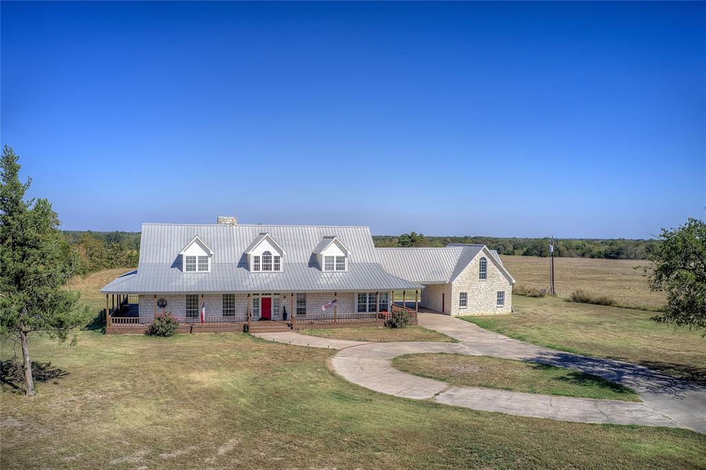 Welcome to your country estate 90 mi from DFW: AG EXEMPT 148 ACRES. A stone-built home w 5 beds and 5.5 baths on 148 ac of rolling pastures and mature hardwoods—blending space, luxury, and rural charm. A large pond enhances the usability of the land, ideal for fishing or livestock. The property is fenced, and includes a 30x10 metal building with a roll-up door. Hunting enthusiasts will love the creek area for exploration with deer and other wildlife. 

This Grand Texas Home boasts a massive wrap-around porch, with a circular driveway, carport, and garage. Step inside to find a light-filled living room with a soaring vaulted ceiling, 2-story windows, a stone fireplace, and doors to back deck. Fresh paint inside and out gives this home a crisp, updated feel. 

The heart of the home is the expansive kitchen, featuring a breakfast bar, massive island with cooktop, granite counters and backsplash, double farmhouse SS sink, double ovens, wine chiller, walk-in pantry. In the spacious dining room, a built-in hutch adds charm, as do bay windows with seating.

The primary suite is a luxurious retreat with two walk-in closets and a private wooden sauna in the bathroom, plus tiled shower with body sprays, toilet and bidet. There is another bed with ensuite bath on the main floor.  Upstairs has two large bedrooms with ensuite baths, built-in dressers, window seats, and recent carpet, with a lofted overlook to the living room below, along with two bonus rooms perfect for game rooms or offices.

The spacious laundry room includes its own shower for added convenience. There's also a half-bath on the main floor. Above the garage, a fully equipped guest suite or man cave offers a wet bar, private balcony, tiled shower bath, lots of storage, and its own AC unit—perfect for long-term guests or home office use.

Recent upgrades include: New HVAC in 2025, LVP Flooring in 2025, Fresh interior & exterior paint in 2025, Carpet upstairs in 2021.