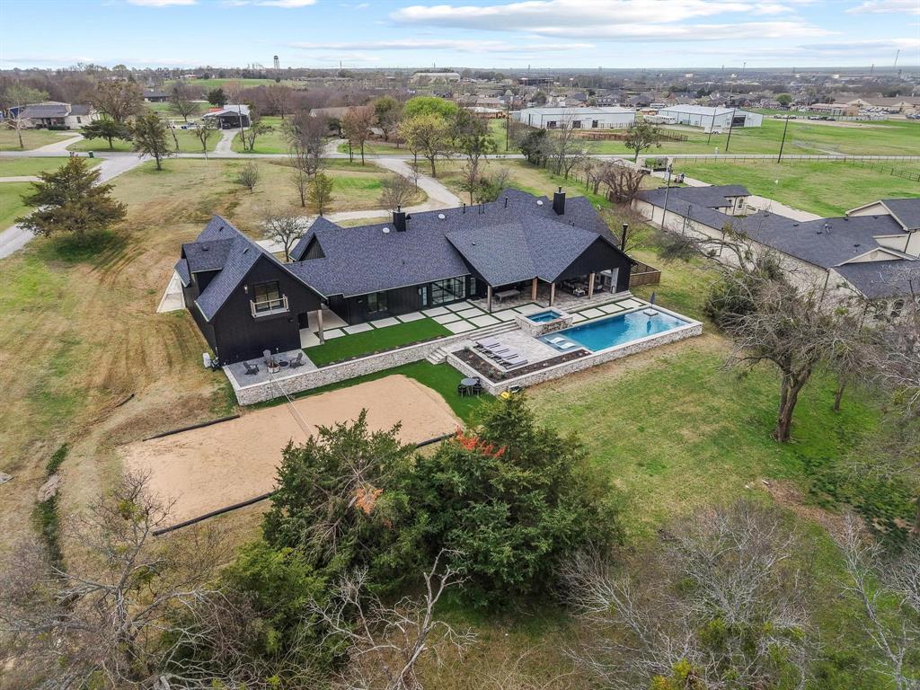 Nestled on 3.44 acres in highly sought-after Gunter ISD, this stunning custom estate offers over 5,065 square feet of thoughtfully designed living space with exceptional indoor and outdoor amenities. With 6 bedrooms, 4.5 bathrooms, and multiple living areas, the home provides both comfort and functionality for everyday living and entertaining.
The main living room features a dramatic stone accent wall, wood-planked vaulted ceilings, and custom iron floor-to-ceiling windows, creating a warm yet sophisticated gathering space. A second living area with a gas fireplace offers additional room for relaxing or entertaining. The home also includes a dedicated office and a spacious laundry room with sink. The chef’s kitchen is designed for both beauty and performance with a 6-burner gas cooktop, double ovens, drawer microwave, built-in nugget ice maker, and Frigidaire Professional built-in refrigerator and freezer. The primary suite is a private retreat featuring his and hers closets and a private patio off the master bedroom. Additional interior highlights include LVT flooring throughout and smart remote-controlled roller shades in all bedrooms. A separate gym space behind the garage with rubber gym flooring provides flexibility for workouts or hobby space, while the upstairs loft offers two open living areas with sink and cabinetry along with a conveniently located half bath.
Step outside to a resort-style backyard designed for entertaining, complete with a 674 sq ft saltwater pool and hot tub, 726 sq ft covered travertine patio, travertine sundeck, built-in grill and outdoor fireplace, sand volleyball court, outdoor shower and turfed gathering areas around the pool and patio. Surround sound speakers throughout the home, loft area, and back patio elevate the entertaining experience. 
This exceptional property with NO CITY TAXES blends luxury living, acreage privacy, and incredible outdoor amenities in one remarkable home.