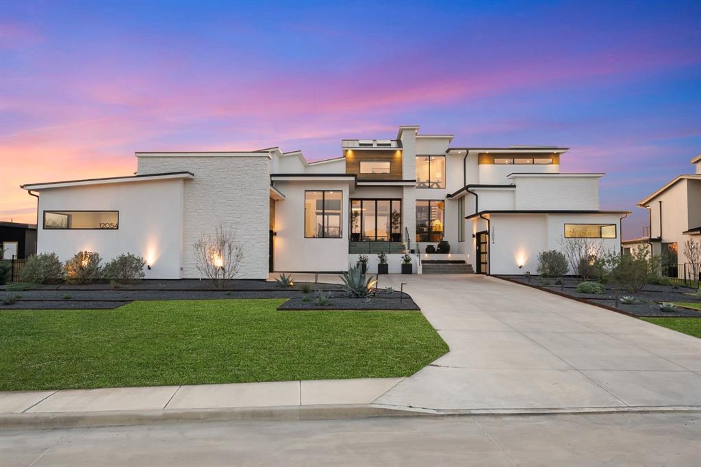 A striking custom-built modern residence overlooking the lake, this one-of-a-kind three-story home blends dramatic architecture, walls of windows and resort-style outdoor living. From the moment you arrive, the clean-lined and perfectly landscaped façade, expansive driveway, and abundant windows create an unforgettable first impression. Inside, soaring ceilings and floor-to-ceiling windows flood the home with natural light and frame beautiful lake views. The main level is the heart of the home, featuring a sunken family room, chef’s kitchen, dining area, and three private bedrooms—each with en-suite baths and walk-in closets. The kitchen showcases an oversized waterfall island, Thermador appliances, gas range, built-in refrigerator, wine fridge, quartz counters and backsplash, and abundant cabinetry. A prep kitchen and walk-in pantry provide exceptional hidden workspace and storage. The expansive main-level terrace creates seamless indoor-outdoor living, offering incredible lake views and a mosquito misting system, perfect for relaxing and entertaining. The ground level features a spacious and luxe game room with wet bar, backyard access, and a full bedroom and bath for guests. The private third level is dedicated to the owner’s retreat with a luxurious primary suite featuring a remote-controlled drop-down TV, spa-inspired bath with soaking tub, oversized shower, and dual vanities. A rare private terrace off the primary suite offers sweeping lake views and a perfect place to enjoy sunrises, sunsets, and holiday fireworks. An adjacent flex space is ideal for a study, workout, or meditation room. Additional highlights include a utility room with dog wash, four garage spaces with storage, tankless water heater, water softener system, remote-controlled front door privacy screen, and French drains on both sides. The backyard is an incredible resort-style retreat with a pool, water feature, turf surround, covered patio, and gorgeous lake views.