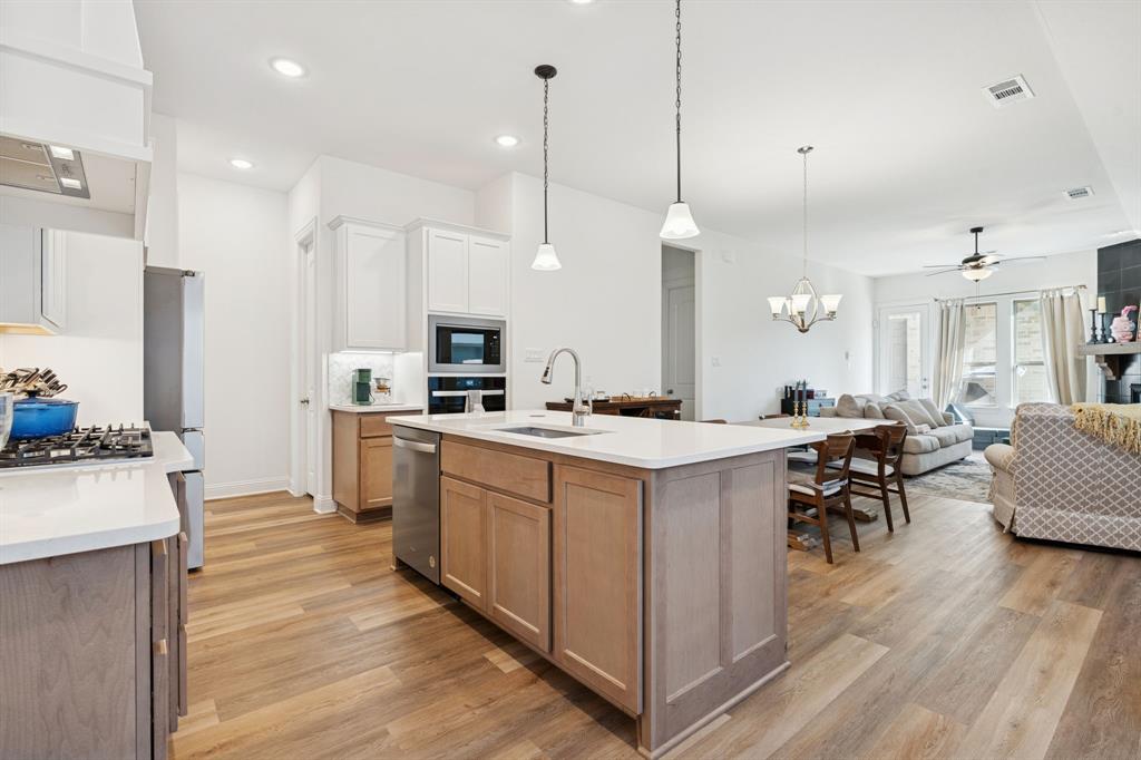 Discover this stunning 2023 Coventry-built home located in the highly sought-after Pecan Square community! This thoughtfully designed 3-bedroom, 2-bath residence offers modern style, low-maintenance living, and access to resort-style amenities. The inviting living area features a ceiling fan, corner fireplace, and open layout perfect for entertaining. The gorgeous kitchen showcases white cabinetry, quartz countertops, a large island with breakfast bar, gas cooktop, and a convenient nook for your coffee bar setup. Luxury vinyl plank flooring flows throughout the main living area, kitchen, and primary suite, while the secondary bedrooms feature plush carpet for added comfort. The spacious primary bedroom includes an ensuite bath with soaking tub, separate shower, dual sinks, and a generous walk-in closet that connects directly to the laundry room with built-in shelving for added convenience. Enjoy outdoor living on the covered patio overlooking a low-maintenance landscaped yard, with a detached 2-car garage providing ample parking and storage. Pecan Square residents enjoy an incredible lifestyle with access to community pools, parks, dog park, fitness area, and tennis or pickleball courts. Experience small-town charm blended with modern amenities in this exceptional home that’s move-in ready and waiting for you!