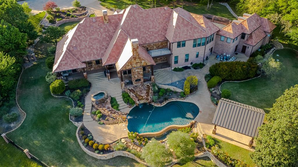 The perfect marriage of rustic warmth and refined elegance, this exceptional cul-de-sac estate sits on nearly two acres, backing to the golf course with sweeping, scenic views. Designed for both everyday living and unforgettable entertaining, the resort-style backyard features an infinity-edge pool with dramatic rock waterfall elements, all surrounded by lush, manicured landscaping that creates a true private retreat within this exclusive 24-7 guarded and gated community. Inside, the home offers a fabulous layout with the majority of bedrooms on the main level. Upstairs, a private suite off the bonus room opens to a balcony with breathtaking views, creating the perfect escape for guests or multigenerational living. A separate guest apartment with its own entrance, kitchenette, and comfortable accommodations serves as a fifth bedroom and offers ultimate flexibility. Entertainment is effortless with media and game rooms conveniently located on the main floor. Car enthusiasts will appreciate the six-car garage and expansive motor court with a remote-controlled gate. Even the details have been elevated, including a heated and cooled 17-foot dog kennel in the garage and a dedicated dog wash station in the utility room. Located in award-winning Argyle ISD and just minutes from DFW Airport, this property offers a rare combination of privacy and accessibility. For those seeking a property that exceeds their expectations, this is the one.