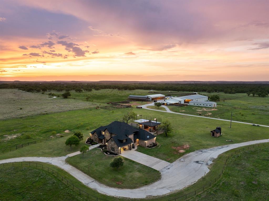 Experience the best of top ranch living in this exceptional custom home and fully equipped equestrian property. A grand gated entrance welcomes you and leads down a scenic pathway to this beautiful custom home and ranch, offering the perfect blend of luxury living and premier equestrian facilities. Step inside to the grand family room, where a stunning wood-burning fireplace and hand-scraped hardwood floors and a pool view you'll enjoy year-round. The gourmet kitchen is designed to impress, featuring a spacious island, natural stone granite countertops, custom stained cabinetry, and stainless steel appliances—perfect for entertaining guests. The spacious master bedroom with sitting area is peaceful retreat after a long day with a primary bathroom with travertine flooring, separate shower, jetted bathtub and dual sinks, The equestrian facilities are truly exceptional featuring two horse barns with 16 total stalls, a show barn complete with a fly system, timed lighting, and heating, plus an 18-stall mare motel. Additional highlights include a 175’ x 100’ indoor arena with convenience of a built in skybox private viewing area overlooking the arena- perfect for cutting, horse pleasure riding and lesson training. Includes a hot walker, 50’ RV barn, 60’ x 120’ equipment barn, trainers office, three wells on property, the livestock wash areas with hot and cold water, couple of tack rooms, and so much more. This remarkable property providing everything needed to support a fully operational with a full cutting training facility and well-equipped equestrian and income producing facility. An exceptional equestrian estate offering peaceful ranch living and just minutes from Fort Worth Metroplex.
