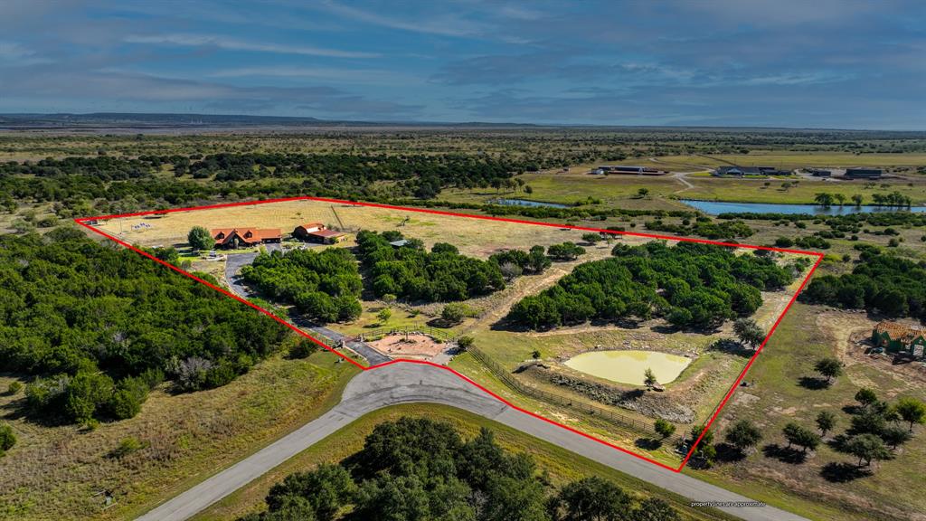 UPSCALE Mountain Spruce Log Home and matching accesory barn sitting on 13 acres in a tranquil ranchette setting at the well-known Possum Kingdom desination lake. This private, stunning oasis has many notable features: vaulted ceiings with structural trusses, open concept living areas,  wrap around porch on all sides of the house, large outdoor covered hot tub, handcarved spruce interior staircase, aspen walls, tongue in groove blue pine ceilings, knotty alder handmade cabinets in kitchen and bathrooms.  Flooring in main living areas is travertine stone. The entire perimeter of the 13 acres is fenced with a variety of fencing but mainly pipe and cattleguard to secure animals from getting in or out of the property. Eight solar panels, 35 ft tall wind turbine, metal roofing, 8 inch thick logs and 12 inch spray foam in all parts of the house make this property extremely ENERGY EFFICIENT. Self sufficient features include a 17 KW generator, two water tanks, rain harvest system, large chicken coop, and a fenced in garden. 12 acres of this property are currently AG EXEMPT and have 3 separate pastures for rotating fields. Most unique features of the barn include an upstairs apartment with a bedroom, full bath, kitchen, dining, washer and dryer hook-up, plus two animal stalls, and a downstairs living area. Perfect for a caretaker for your horse farm. This lake ranchette currently has boar goats, chickens, and donkeys. The pond sitting area is a serene place for animals to drink and for you to enjoy the sunset while feeding the fish on the metal framed dock with Trex boards. Fire pit by home faces west to unwind with the nightly sunsets and the dark skies you will find here in North Texas. UPSCALE AMENITIES to boot- community clubhouse with fitness center with commercial grade equipment and an infinity swimming pool overlooking the lake. Community lake cabin with dock & watercraft launch. And, much more. This UNIQUE listing has it ALL. Must see in person to fully appreciate!