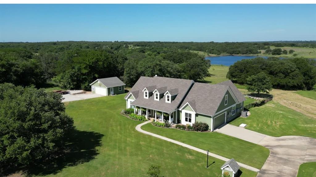 Primarily one-story home on just over 3 acres provides ideal space for hobbies, equipment, gardening, or simply enjoying the privacy and views around the lake. Adjacent 3 acre tract also available (MLS #20877045). Purchase both properties together for approximately 6 acres total. This energy efficient home has 60 OWNED solar panels and battery backup designed to offset most, if not all, of the electric bill. All main living areas and bedrooms are downstairs with only a private guest suite and full bath upstairs. This 4 bedroom plus office, 3.5 bath home offers 2,550 sq ft with high ceilings, oak flooring in the living and dining areas, tile in the kitchen, baths and halls, with vinyl picture windows throughout. Living room features a gas fireplace with granite surround. Kitchen includes custom maple cabinetry and granite countertops and opens to both the living and breakfast area. Dedicated office with built-in desks. Private primary suite with safe room & storm shelter closet. Two bedrooms share a Jack & Jill bath with granite countertops, while the upstairs bedroom and full bath offer a private space ideal for guests or multigenerational living.  Walk-in floored attic offers excellent storage. Structural Insulated Panel construction for added efficiency. Central vacuum. New AC in 2023 and upstairs mini split in 2022. Roof replaced in 2025. Backyard designed for entertaining with resort-style pool featuring infinity edge, fountains, slide, lighting and new filter (2025), upper and lower concrete pool decking, covered back porch, fenced yard, raised garden beds with drip irrigation and deer fencing, and sprinkler system with Tifway 419 Bermuda grass. Additional features include fiberglass tornado shelter that will seat 6, greenhouse with a 1 car garage, an additional detached 2 car garage & workshop, RV pad with electric hookup, concrete driveway, and water well for irrigation.