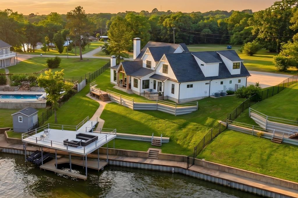 If you’ve been waiting for the right lake house—this is it. Elevated above Cedar Creek Lake with sweeping open water views, this modern farmhouse delivers the rare combination of newer construction, thoughtful design, and true lake lifestyle just over an hour from Dallas.

Built in 2021, the home offers 5 bedrooms, 5.5 baths, and approximately 4,488 square feet designed for both everyday living and large gatherings. The open-concept main level features warm wood beams, shiplap accents, a floor-to-ceiling stone fireplace, and walls of windows that bring the lake into every moment. The chef’s kitchen is built to entertain with quartz countertops, an oversized island, premium appliances, bar closet, and walk-in pantry.

The primary suite is a private retreat with private patio and water views, while a main-floor study easily functions as a guest suite. Upstairs, two generous guest bedrooms with en-suite baths and a dedicated recreation wing with built-in bunks, game room, full bath, and additional bedroom create the perfect setup for hosting family and friends.

Outdoor living takes center stage with a wraparound covered porch, porch swings, outdoor fireplace, and grilling area overlooking the water. The fenced yard slopes to a private boathouse featuring a 25-foot slip, dual jet ski lifts, and a sunken party deck—designed for long weekends and sunset evenings.

Located in Arnold Hills with access to a pickleball court and private boat ramp, this is more than a home—it’s the lake lifestyle buyers are searching for.