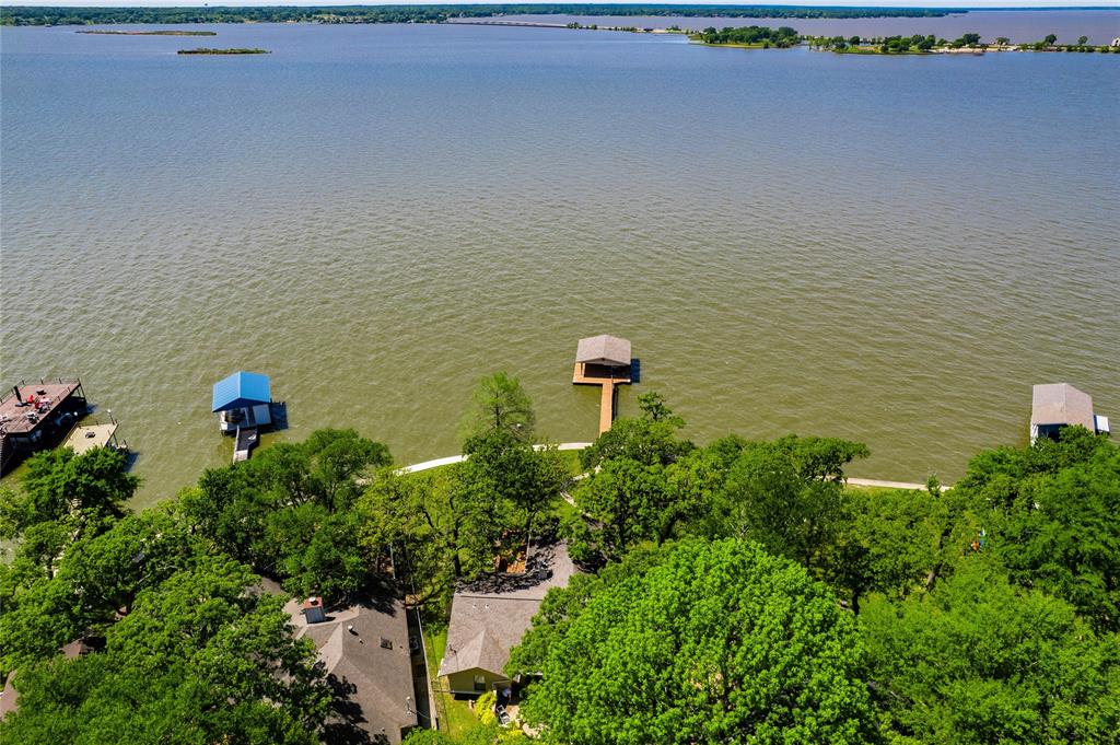 Fantastic Private retreat on a large, tree-filled lot with expansive open water views.  Designed for lakefront living, this homes features a spacious covered porch and extensive decking, perfect for soaking in the scenery.  A boathouse with personal watercraft lift makes enjoying the water effortless.  Inside, the open-concept living area boasts vaulted ceilings, a fireplace, and a wall of windows, bringing in natural light and panoramic lake views.  Entertaining is seamless with a beverage bar serving both indoor and outdoor spaces.   The dining area overlooks the water, creating a stunning backdrop for every meal.   The private owners suite offers lake views and opens onto its own secluded deck.  Generous-sized bedrooms ensure comfort for family and guests.  With a two car garage and ample parking, this property is ready for unforgettable gatherings.