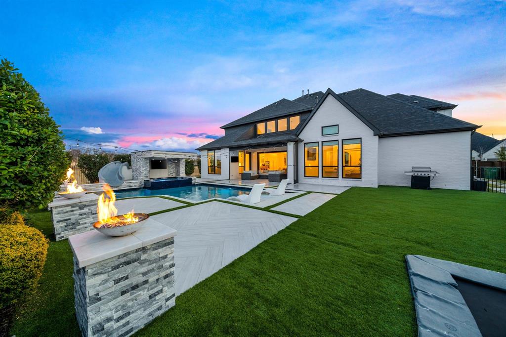 Positioned on a premium corner lot across from green space in Windsong Ranch, this exceptional home blends luxury upgrades with resort-style outdoor living. Thoughtfully crafted for both entertaining and everyday comfort, the home showcases designer lighting, hardwood flooring, motorized shades, soaring ceilings, and decorative wall paneling that add warmth and architectural character throughout. A dramatic entry welcomes you with a sweeping staircase, along with a glass-enclosed study and separate fitness studio. The expansive living area is filled with natural light and highlighted by a floor-to-ceiling tile gas fireplace, while oversized accordion glass doors seamlessly connect the indoor and outdoor living spaces. The chef’s kitchen is beautifully appointed with an oversized island, double ovens, built-in refrigerator, pot filler, custom glass cabinetry extending to the ceiling, and designer brass hardware. A spacious butler’s pantry with a built-in wine refrigerator adds convenience and functionality for entertaining. The open-concept layout flows seamlessly into the dining and living spaces. The downstairs primary suite offers a private retreat overlooking the backyard with vaulted ceilings, a soaking tub, double-entry glass shower, separate dual closets, and direct backyard access. A secondary ensuite bedroom is also located on the main level, ideal for guests or multigenerational living. Upstairs features three additional ensuite bedrooms, a spacious game room with built-in media space, and a separate media room. The backyard is designed for year-round enjoyment with a fully turfed yard, heated pool and spa, water features, slide, tanning ledge, in-ground trampoline, covered patio with automatic screens, and multiple outdoor seating areas. Residents also enjoy Windsong Ranch amenities including the crystal-blue lagoon, tennis courts, paddle boarding, trails, community events, and more.