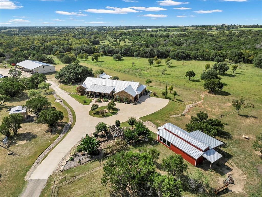 Tucked away on 42 picturesque, fully fenced acres, this legacy property with multiple homes, is the ultimate blend of Texas charm and modern convenience. The main lodge-style home spans 3,842 sq ft, boasting 4 bedrooms, 3.5 baths, a massive office, and gorgeous stone-accented walls that bring the outdoors in. Wide 3-ft doors add accessibility, while the backyard oasis will steal your heart, complete with a sparkling pool, water features, and a cabana with a roll-up door made for entertaining. Got toys or a trade? The 4,000 sqft shop with a 16-ft porch has you covered, and the 24x50 barn is ready for your next venture. There’s also a stocked pond, a massive garden with grapes, squash, zucchini, apple trees, peach trees, plum trees, 
banana trees, tomatoes, jalepenos, roses, and more. The beautiful hardwood trees throughout, with Squaw Creek bordering most of the back of the property make this property nearly irreplaceable. A second home, a spacious 2,450 sqft double-wide with porches on both sides—offers 4 beds and 2.5 baths, perfect for guests or multi-generational living. Wildlife seen on the property includes but not limited to whitetail deer, doves, ducks, geese, wild turkeys, owls, bats, bobcats, foxes, coyotes, various birds and more. Add in the grand gated entrance, and you've got a one-of-a-kind property built to be passed down for generations.