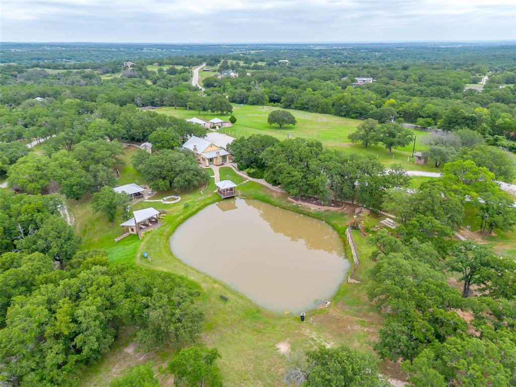 Conveniently located 36 miles of downtown Fort Worth & Stockyards this 39.26 acres of improved and natural ranch land offering privacy, versatility, and wide-open potential. Six of the 39.26 acres is cross-fenced pasture under wildlife exemption. Behind two gated entrances, the land opens into a blend of softly groomed areas and native terrain, with improved roads, walking and riding trails, gazebos, pergolas, and a private stocked pond designated for catch-and-release fishing. The architectural style blends classic ranch character with Mediterranean influence. Residential improvements include four separate homes. The main residence offers three bedrooms and two baths with an open-concept layout. A second home provides a one-and-a-half-story design with two bedrooms, two baths, a fireplace, and a warm cabin feel. The third residence features a two-bedroom, two-bath open layout, while the fourth is a one-bedroom, one-bath open-concept home. Two duplex-style buildings add four studio or efficiency units suitable for guests or supplemental income. Additional improvements include an office building with restrooms and breakroom, a pool house with restrooms, a barn, and a large multi-purpose structure with two fireplaces, a full kitchen, and two outdoor showers. These improvements are connected by natural courtyards and walkways, creating a functional and cohesive ranch compound. Outdoor amenities include a commercial-style pool with gazebo, half-court basketball, soccer field, putting green, life-size chess set, grotto, fire pits, and seating areas positioned throughout both open and wooded portions of the land. The property also includes a storm shelter, multiple sheds and outbuildings, and ample room for additional agricultural, residential, or recreational improvements. Multi-generational family compound, private farm and ranch estate, or income-producing property. Conveniently located 36 miles of downtown Fort Worth & Stockyards.