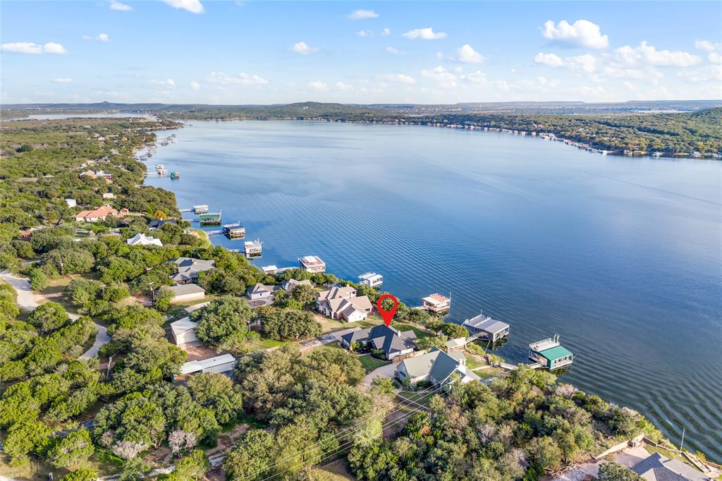 ALL the essential features savvy buyers seek are found in this stunning lakefront estate on the big open main body of Possum Kingdom Lake. Enjoy premier southern exposure, breathtaking panoramic views over crystal-clear, 60-foot deep waters, right across from Sandy Beach — an unbeatable location for recreation and long-term value. This property is a dream for boating enthusiasts, featuring a newer full-sized double-decker dock with durable composite decking, three slips & boat lifts, all situated in deep water. Enter through a private gated drive to a beautifully manicured estate with lush lawns, mature shade trees, and an oversized, park-like setting. Ample asphalt parking offers convenience for guests or gatherings. Inside, the main home boasts huge bedrooms, a spacious open living area with fireplace, and wall-to-wall lake views. Recent upgrades include new windows, doors, roof, and more, giving peace of mind for years to come. A covered outdoor living area lets you entertain or unwind while taking in those incredible lake vistas and cool southern breezes across the large grassy backyard with room for a future swimming pool. The property also includes a detached guest quarters with a full bath and double carport — perfect for visitors. Both main house and guest quarters are offered fully furnished, it’s truly turnkey, ready to enjoy immediately or leverage as a luxury rental. Whether you’re looking for a full-time lakefront residence, a private family retreat, or an investment property in a popular resort community with all the must-have features — deep water, premier dock, spacious land, privacy, and updated living — this estate delivers exceptional value and lifestyle on Possum Kingdom Lake.