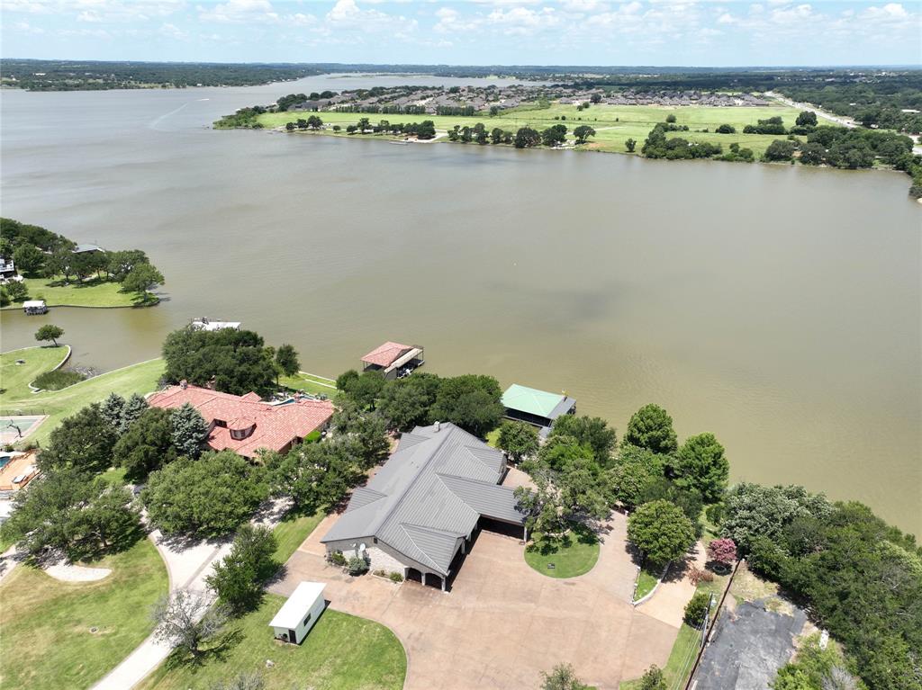 OWN A RARE PIECE OF PARADISE.   Sprawling 1 acre Main body Lake Front property, situated behind private gate with guest house, workshop, & abundant storage. Large circle drive welcomes you into this stately stone & tile roof estate featuring, iron fixtures, cathedral ceilings Parque & ceramic tile flooring, with encompassing windows throughout. Prepare meals in Chefs eat-in kitchen w-unending rich wood cabinetry, DBL oven, granite counters, island, pantry & overlooks living with showpiece fireplace & wood beams. 2X Master suites boasting seating area & ensuite bath complemented by dual vanities, jetted tub, separate shower, and oversized walk-in closets. Additional features include sitting room, 2X gun closets, cedar closet, enormous utility room with storage, island, and sink. Recent updates include:  fresh interior paint, new flooring, landscaping, tree trimming for lake visibility. Sip coffee on multiple stained concrete covered porches or under pergola w- water views. Have fun on water with 2 story Trex boat dock w- lift, slide, private boat launch & beach side gazebo situated in very deep water on Lake Granbury. Large covered parking, 2 car garage & storage area for boats. Just 2 miles from historic square shopping & dining.  This exquisite lakeside hideaway is a must see and easy to show!