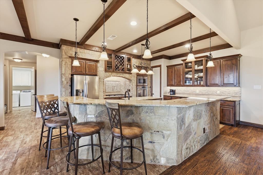 The fireplace on the covered patio gets more use than the one inside. Stone surround, ceiling fan, mounted TV. In North Texas, that's ten months of morning coffee, dinner outside, and evenings you don't want to end. That is if you can find the strength to leave your kitchen. Tuscan style stone-wrapped range alcove, granite island, bar seating, built-in wine rack, double oven, and wood beam accented ceiling. The dedicated home office opens with double barn doors and has its own closet. The main bathroom, with dual vanities, has a huge closet, walkthrough shower with dual heads and a soaker tub, for those days you need to unwind. And you haven’t even seen the true 3-car garage with an extended truck bay, spray foam insulation, hardwood floors, a huge half-acre yard, vaulted ceilings with wood beam trusses, and a floor to ceiling living room fireplace. Book your showing.