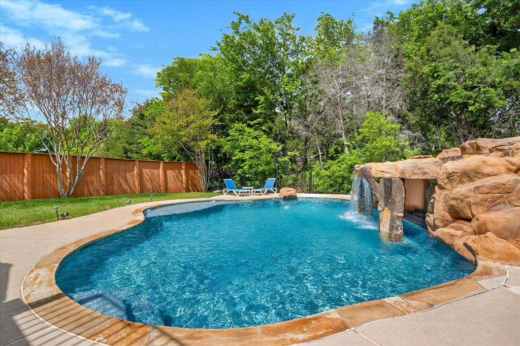 Lender buydown options available on the home! Paradise found with this amazing home with resort style pool on incredible private lot overlooking towering trees & green space. This immaculately maintained home offers the perfect combination of comfort, charm, & practicality, providing everything to day’s family needs for relaxed living & effortless entertaining. Your home will be the place to host the pool party with its resort style pool complete with swim up bar and grotto! Step through the front door & into a spacious, flexible front room that can be tailored to suit your lifestyle – whether that’s a formal dining area, cozy second lounge, or contemporary office. A standout feature is the custom-built bookcase, which cleverly conceals a hidden storage space – a rare & thoughtful detail that adds both character & function. Rich hardwood flooring creates a warm & welcoming atmosphere. The contemporary kitchen is the heart of the home, boasting stainless steel appliances, elegant cabinetry, & modern lighting. It opens seamlessly into a bright sunroom – perfect for family meals or enjoying a quiet coffee or simply unwinding in the natural light with incredible views of the outdoor living space. The expansive primary suite offers a peaceful retreat with sitting area & private balcony overlooking the beautifully landscaped yard. The outdoor space is truly exceptional & perfect for entertaining or relaxing. Access to pool bathroom just inside the home is an added bonus! Three auxiliary bedrooms offer excellent flexibility for children, guests, or space to work from home. The air conditioned  third-car garage is a bonus, ideal as a home gym, workshop, or office. Spacious laundry room includes laundry shute from upstairs. Extended drive and 3 car garage provides ample parking space for family & friends! Located near Rockwall's great schools, restaurants & near major highways makes it a must see!