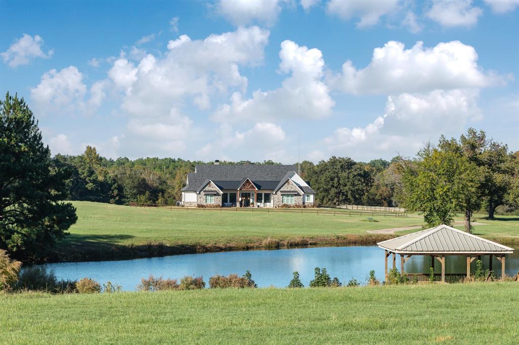 72-acre JH Ranch is in East Texas near Lindale, TX. The stone gated entrance leads to ranch home surrounded by pipe fencing sitting on a hillside overlooking pastures, pristine hay meadows, 2-acre fishing lake with Gazebo covered pier. The 3339 SQFT ranch home includes emergency generator. Open design with spacious great room, vaulted ceiling and corner fireplace. Dining area breakfast bar gourmet kitchen gas cook top double ovens microwave walk-in pantry. 4-bedroom 3-bath ranch home room for family and guests. Master suite bedroom is large Master bath Oversize shower, garden tub, water closet, double sinks, and walk-in closet. The covered back porch includes fireplace, outdoor kitchen, ceiling fans, TV and sitting area. The land has a gentle roll with large oaks scattered about. The hay meadows provide quality horse hay. 30 ft x 60 ft steel building with concrete floor, roll up doors on each end and 15 ft overhangs on each side provides plenty of space. Cattle working pens.