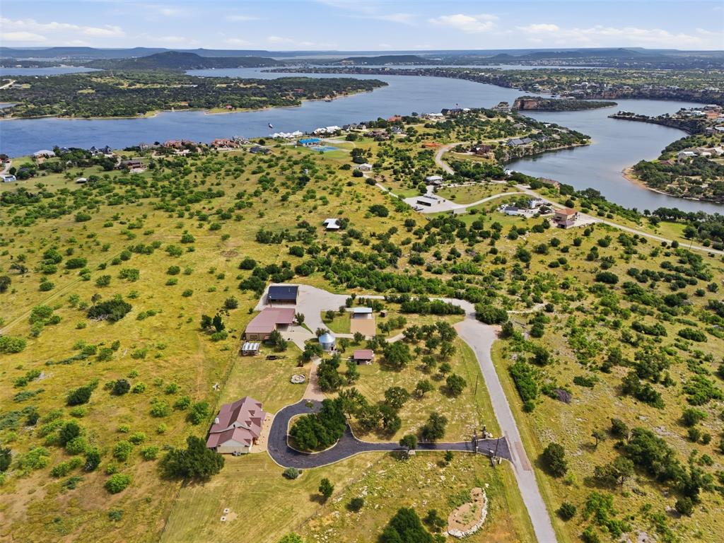 Welcome to Mi Dia Ranch, a rare 20-acre estate in the heart of Sportsman’s World at Possum Kingdom Lake where ranch living, entertainment and lake life collide! This turn key estate is fully built-out, furnished and was designed with intention. It offers a unique opportunity to own not just a home, but a destination & proven gathering place. The main residence is thoughtfully designed around a central living, kitchen, and dining space with vaulted ceilings and rich custom finishes. On each side of the home you’ll find private, stand-alone primary suites, each with its own entrance and porch creating a true retreat experience for owners and guests alike. Beyond the main home, the property transforms into an entertainer’s dream. The party barn features spacious living & dining areas, a commercial-grade kitchen, upstairs loft and shop. At the center of the property you will find the iconic Silo bar that delivers a one-of-a-kind experience complete with a fully outfitted bar, lounge area, & loft bedroom creating an unforgettable atmosphere. A covered stage with professional sound equipment is ready for live music, private concerts, movie nights, or gameday gatherings. Having hosted both local & national bands, this property is already established as a destination for events & celebrations. The outdoor pavilion kitchen & living area is designed for connection & comfort, featuring a rustic farm table, smoker, pizza oven, grills, and a stone fireplace.  A greenhouse, firepit and a newly constructed RV & boat storage barn offering space for all your lake & ranch lifestyle needs. Located just down the street from Bluff Creek Marina & Hell’s Gate, this property offers convenient access to one of Texas’ most iconic lake destinations. Mi Dia Ranch offers endless possibilities: a private retreat, income-producing venue, corporate getaway, or legacy property. Few properties deliver this level of versatility, privacy & experience all under those famous PK sunsets!