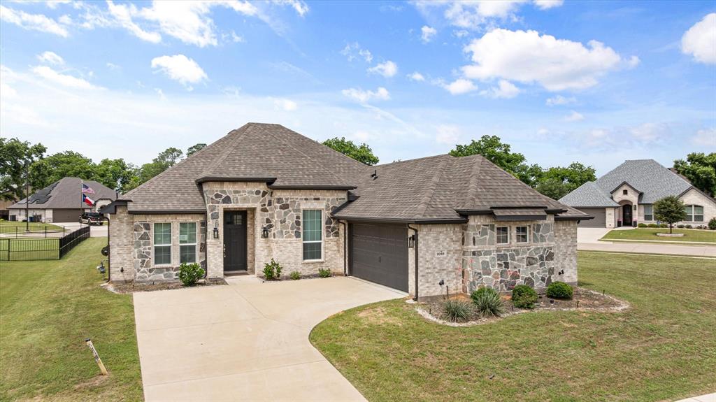 Discover the perfect blend of modern elegance and small-town charm in this stunning brick-and-stone home located on a corner lot in Granbury's highly desirable gated Harbor Lakes community. This single-story home offers 3 bedrooms, 2 baths, an office near the front entry with a closet that can easily serve as a 4th bedroom, a 2-car garage, and an open-concept floor plan. The eat-in kitchen features granite countertops, stainless steel appliances, abundant cabinetry, and a large center island with sink and breakfast bar, all opening to the spacious living area with a corner fireplace. The primary suite offers dual vanities, a garden tub, separate shower, and a generous walk-in closet. Conveniently located with easy access to shopping, dining, everyday conveniences, and major highways. Enjoy quick access to Lake Granbury's boat ramps, parks, and waterfront dining, while the award-winning Historic Granbury Square is just minutes away, offering boutique shopping, local restaurants, live entertainment, and year-round community events.  All measurements, square footage, and school information are approximate and should be independently verified. This property is owned by the Secretary of Veterans Affairs and is being sold AS IS. Visit VRMProperties for more information.