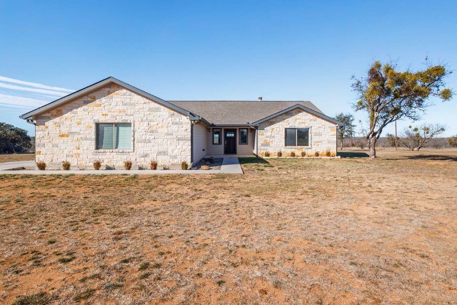 Set on 14 scenic acres just minutes from town, this white stone home offers the perfect blend of peaceful country living and everyday convenience in the highly desirable Early ISD. Located outside city limits, the property provides room to grow with space ideal for livestock, 4-H projects, and recreation.
The 3-bedroom, 2-bath home features an open, light-filled floor plan with vaulted ceilings and a wood-burning fireplace anchoring the living room. The kitchen opens to the living area and is highlighted by marble countertops, ample cabinetry, and an inviting layout ideal for gatherings. Marble countertops continue throughout the home, including all bathrooms.
A chandelier accents the dining area, which includes custom built-in display cabinets, drawers, and a wine rack. All bedrooms offer walk-in closets with built-in shelving. The private primary suite features vaulted ceilings and a spacious bath with dual sinks, a jetted soaking tub, and a large glass-and-tile walk-in shower.
Step outside to the covered back porch and enjoy views of rolling hills, mature trees, and abundant wildlife. The fully fenced acreage includes Zephyr water and an additional construction pad with road, gate, and separate power meter for future expansion. Finished two-car garage, decked attic storage, enhanced foundation, and fiber-optic internet complete this exceptional property.