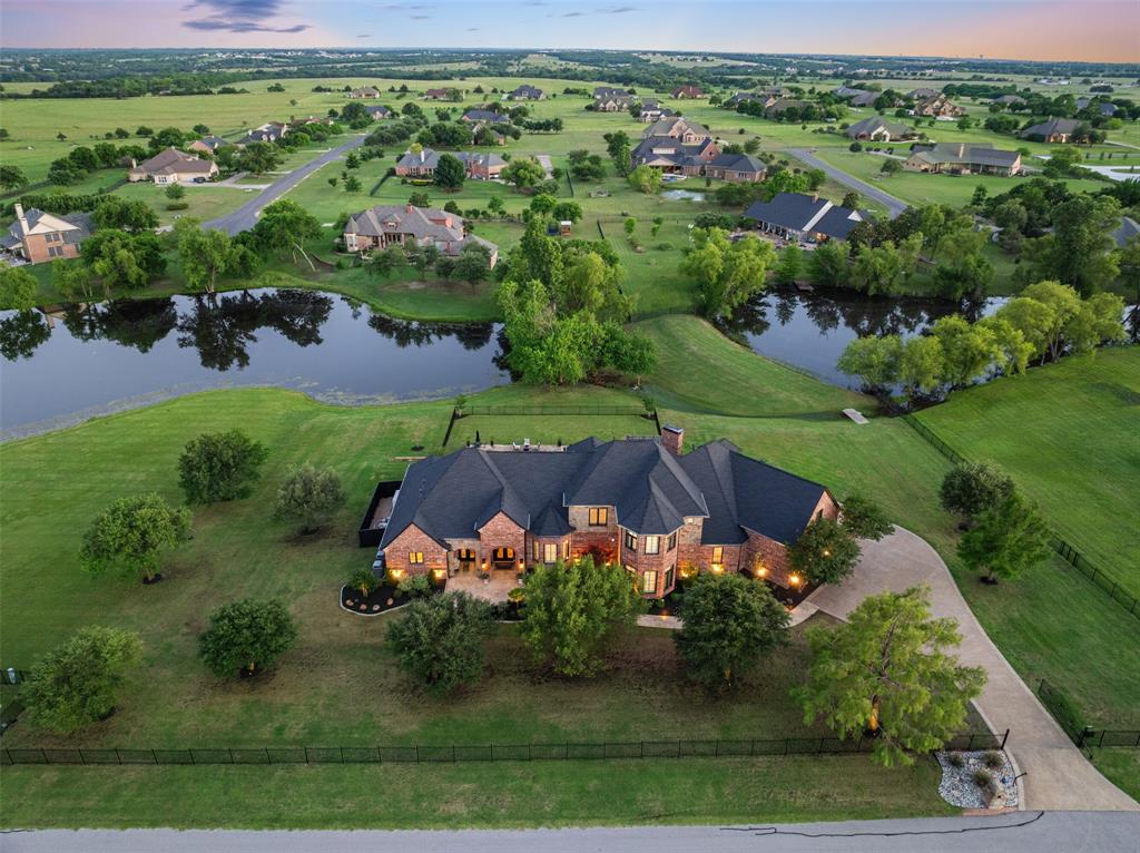 Are you searching for a tranquil place to call home? Nestled on more than two acres just five minutes from Preston Road and Downtown Celina, 4750 Lake Drive offers an exceptional blend of luxury, comfort, and breathtaking views. This stunning 5,424-square-foot gated estate overlooks a trio of lakes and was thoughtfully designed for both everyday living and effortless entertaining.
From the moment you step through the double wrought iron doors, the home makes a lasting impression. A grand foyer featuring herringbone floors and a barrel ceiling sets the tone for the quiet elegance found throughout.
The chef’s kitchen is sure to inspire your culinary creativity with custom cabinetry, a statement range hood, and premium Thermador appliances, including a 60-inch range, built-in coffee maker, and wine refrigerator. The kitchen and dining spaces seamlessly open to the outdoor living area, where an expansive patio, outdoor kitchen, and infinity-edge pool showcase spectacular lake views.
Designed with entertaining in mind, the home offers three distinct gathering spaces: a sunken great room, an upstairs game room, and a dedicated entertainment area complete with a wet bar.
With five bedrooms and five bathrooms, there is room for everyone to enjoy both comfort and privacy. The downstairs guest suite is ideal for visitors, while three additional bedrooms are located upstairs. At day’s end, retreat to the luxurious primary suite featuring a sitting area, custom closet, and spa-inspired bathroom designed to be a sanctuary of relaxation.
Every room has been thoughtfully curated to balance beauty with functionality, creating spaces that are as livable as they are impressive. Situated on a quiet cul-de-sac with friendly neighbors, this remarkable property is more than a house — it is a place to truly call home.
